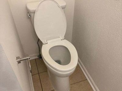 A white toilet with the seat up in a small bathroom. The floor is tiled, and the walls are plain.