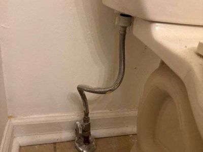 A toilet's flexible water supply line with a kink, connecting the tank to the shut-off valve near the base of a white wall.