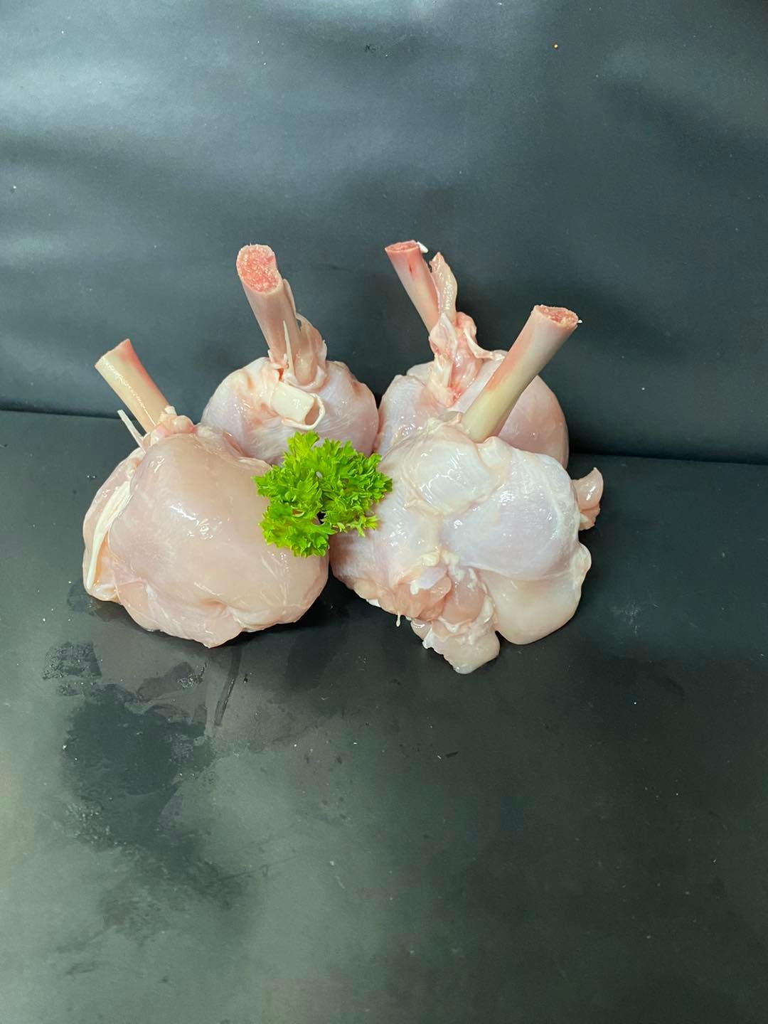 Two Raw Chicken Wings With Parsley on a Black Surface — Fresco's Quality Meats (Retail) in Mount Isa, QLD