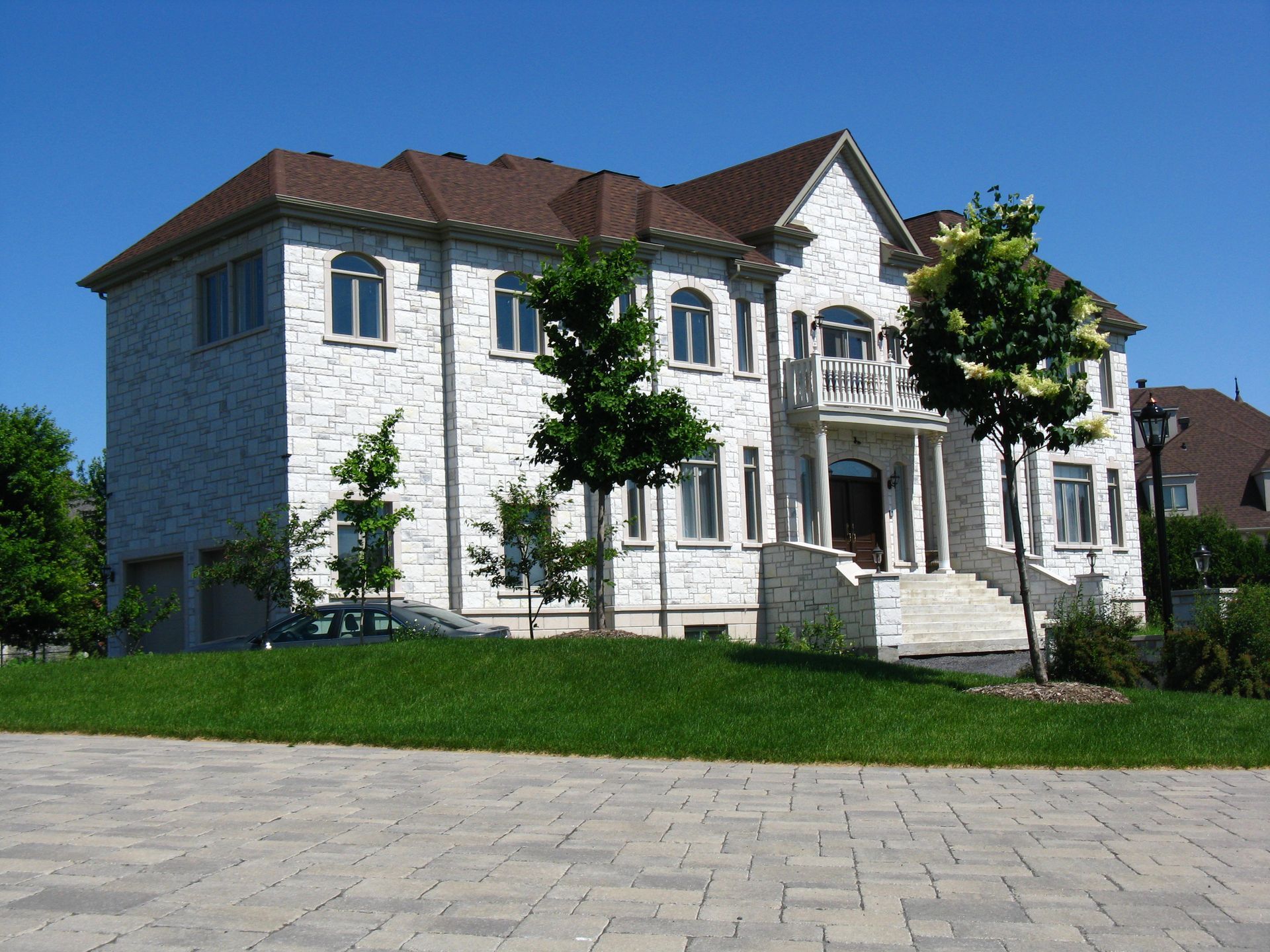 Maison de deux étages en briques blanches avec toit marron, pelouse verte et ciel bleu.