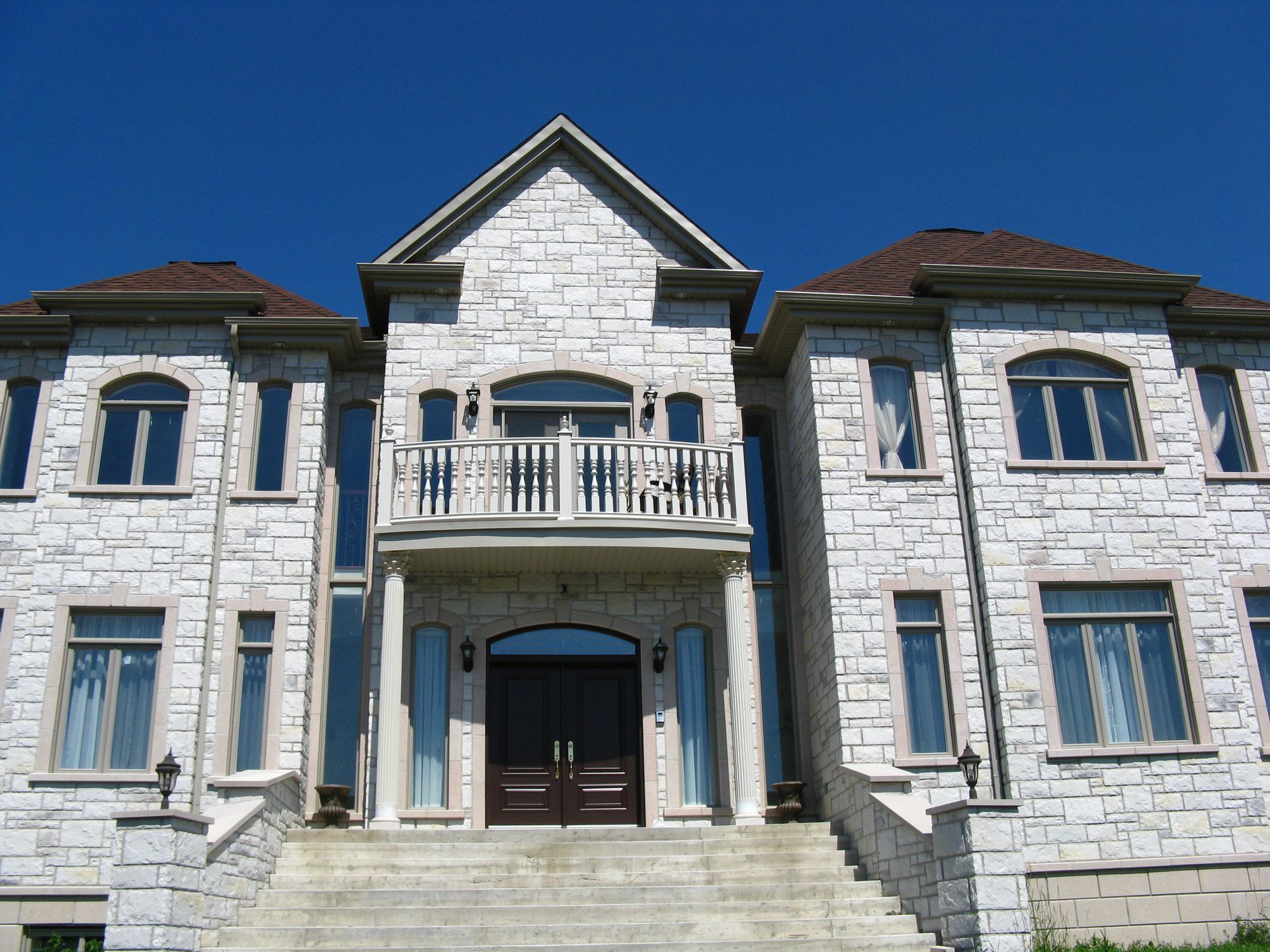 Maison en pierre de deux étages avec balcon et portes brunes se détachant sur un ciel bleu.