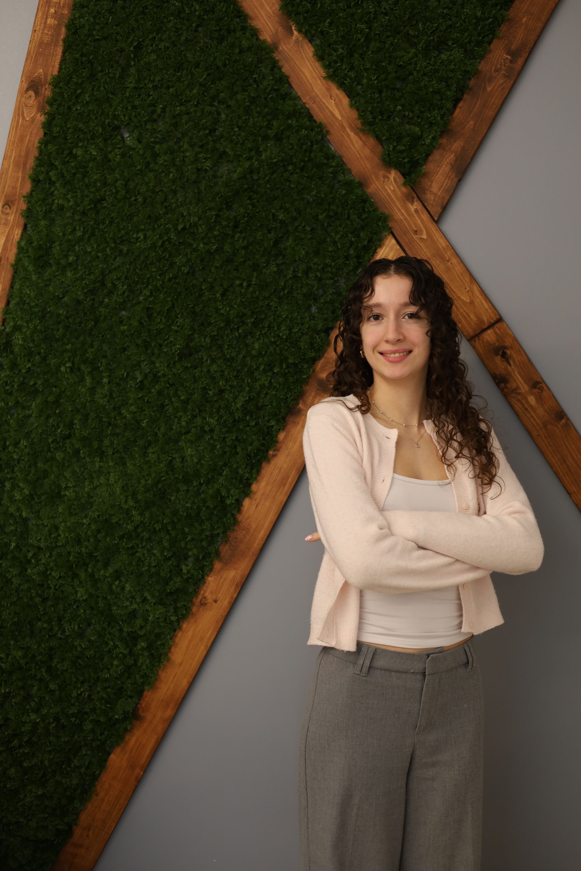 Femme les bras croisés, souriante, vêtue d'un t-shirt noir et d'un jean, devant un mur bleu.