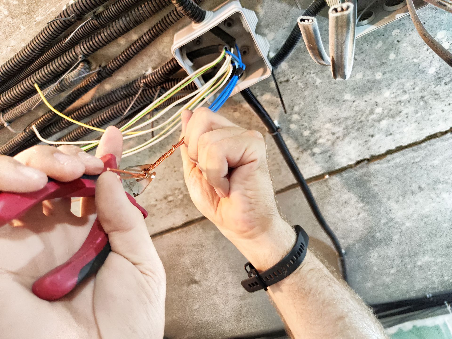 Electrician working on wiring in a residential garage during daylight hours using wire strippers.