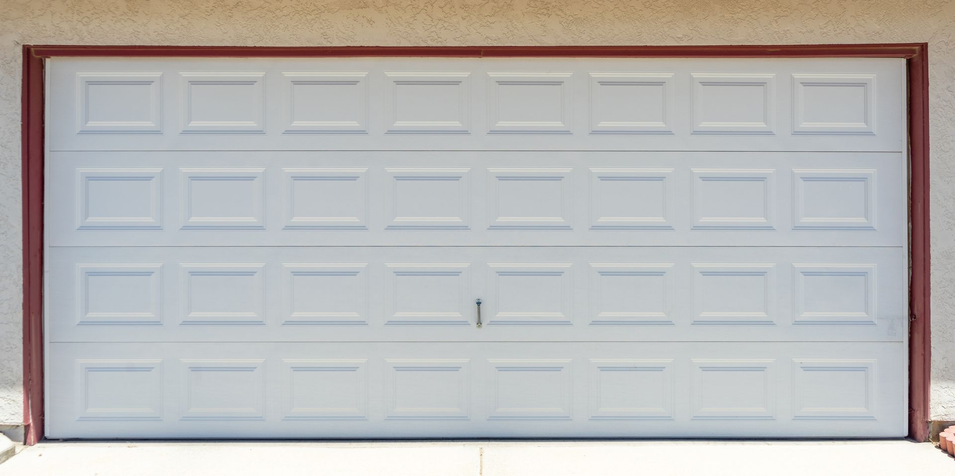 Closed white sectional garage door framed by red trim on a residential exterior wall in daylight