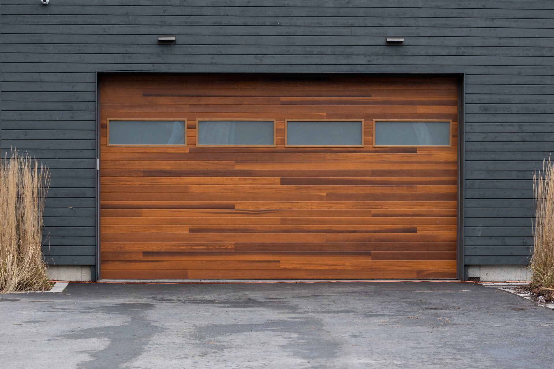 A modern brown faux wooden exterior garage door with four small horizontal glass windows.