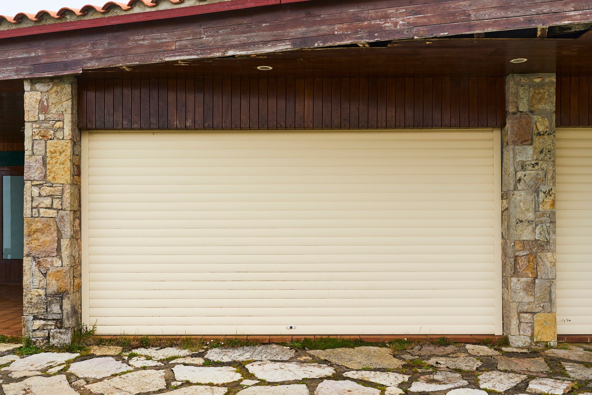 Closed beige garage door with stone pillars and wooden paneling. Closed beige garage door with stone pillars and wooden paneling.
