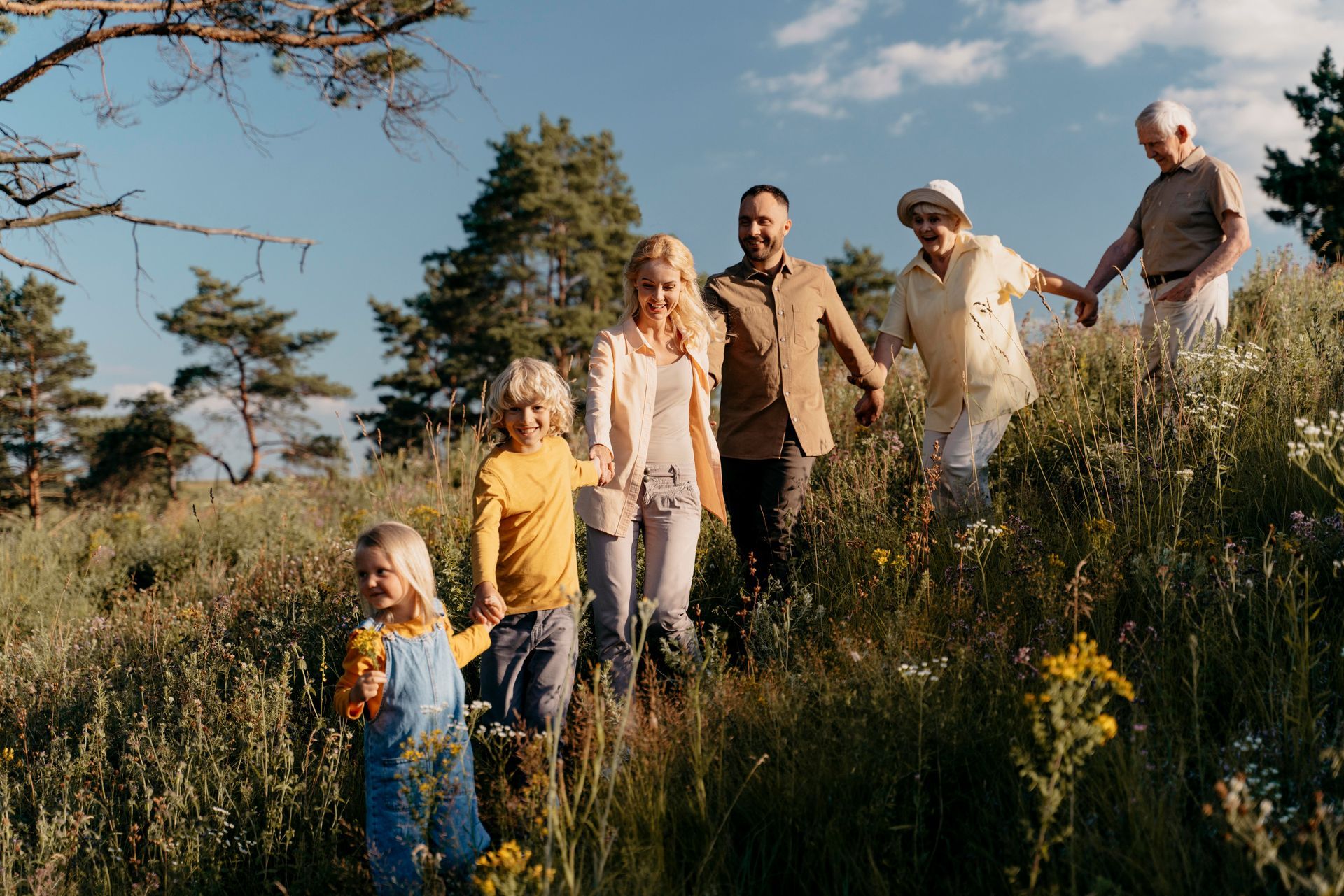A family is walking through a field of tall grass holding hands.