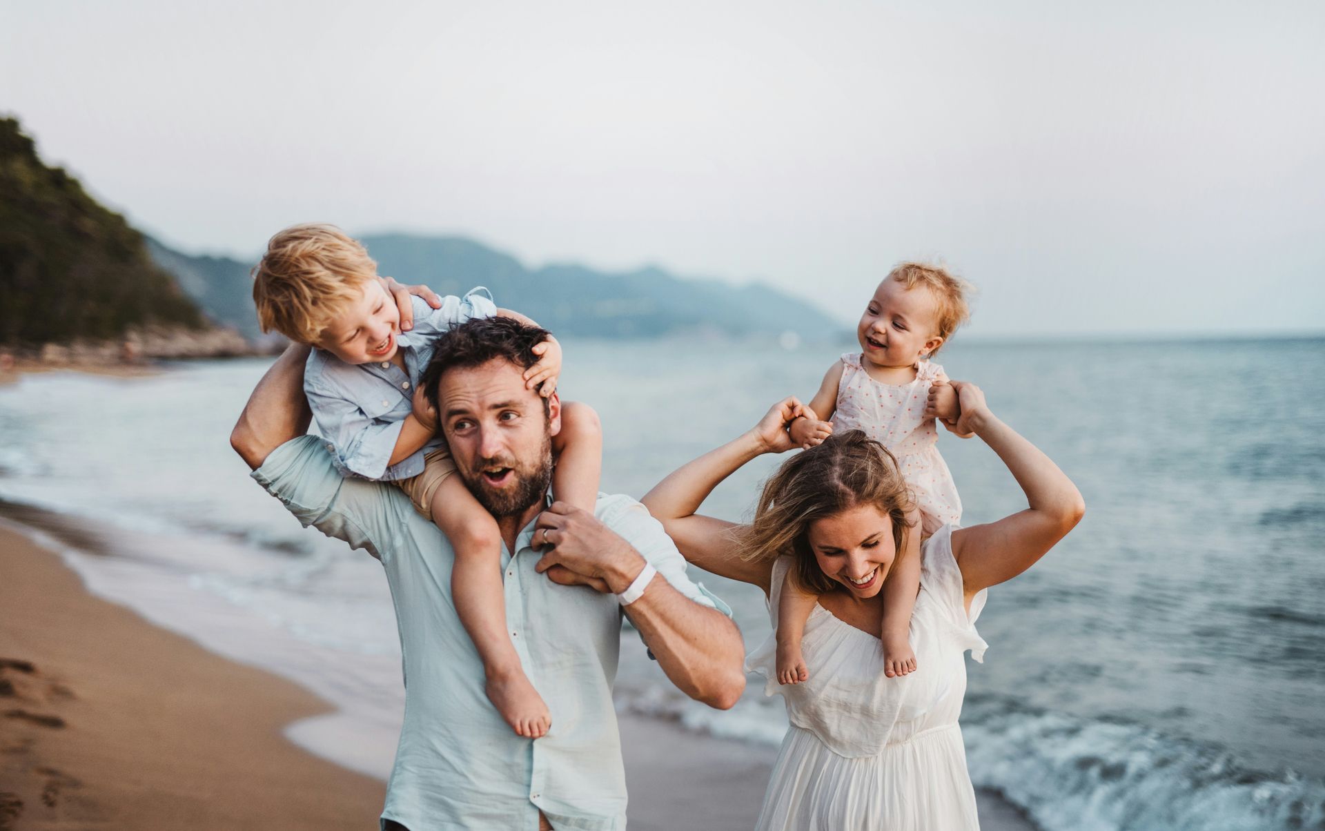 A family is standing on the beach holding their children on their shoulders.