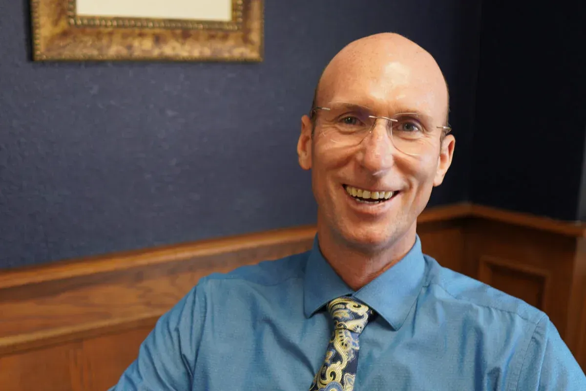 A bald man wearing glasses and a blue shirt is smiling for the camera.