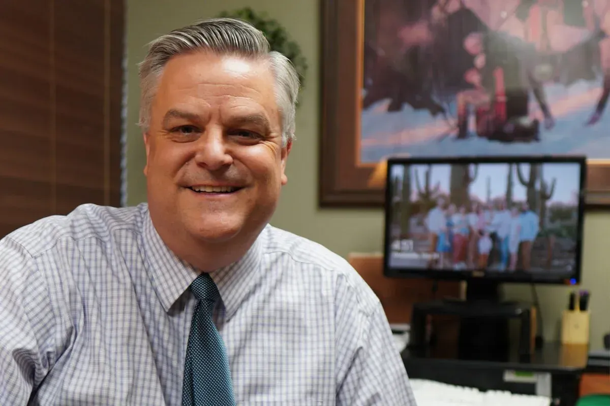 A man in a plaid shirt and tie is smiling in front of a television.