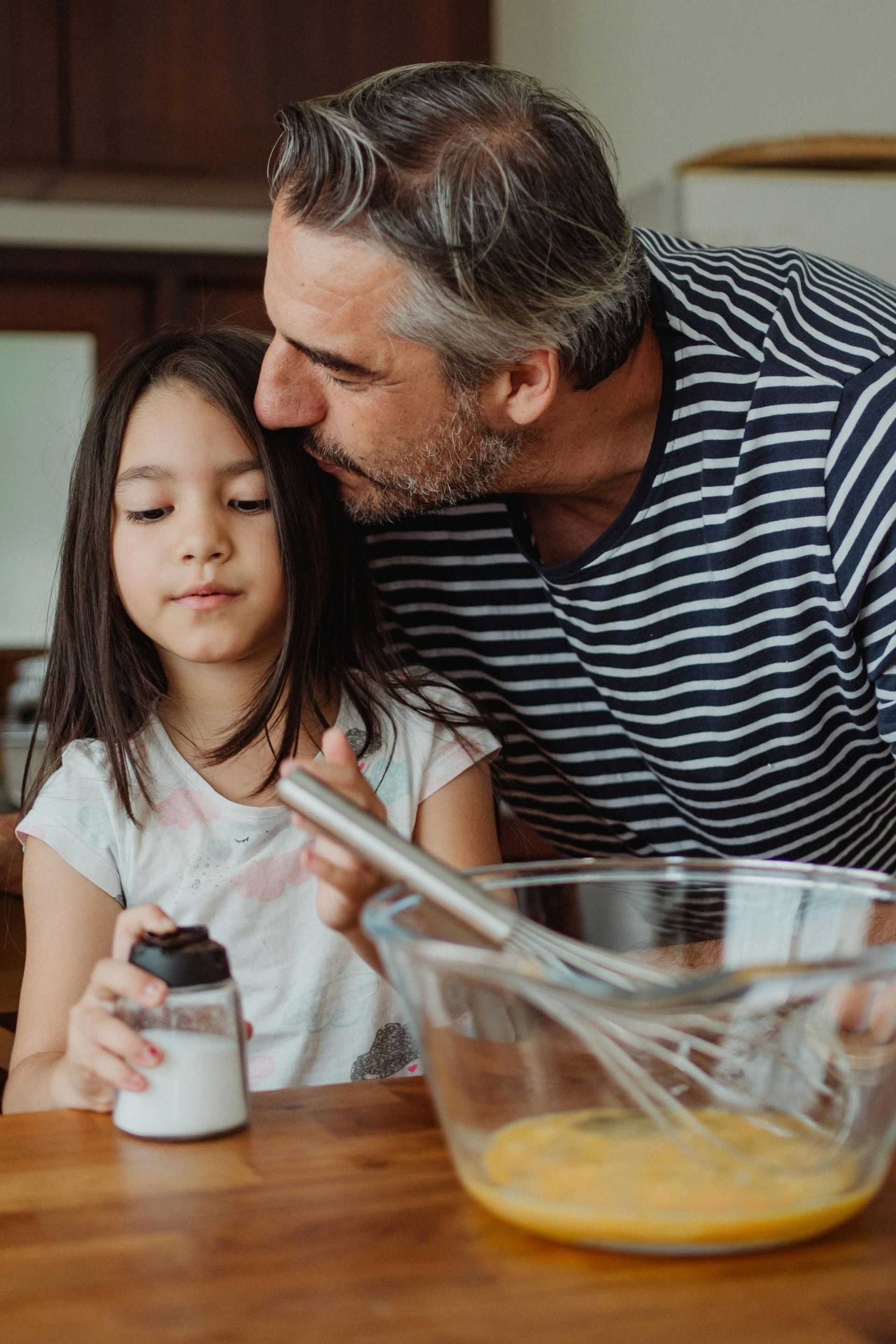 A man and a little girl are preparing food in a kitchen.