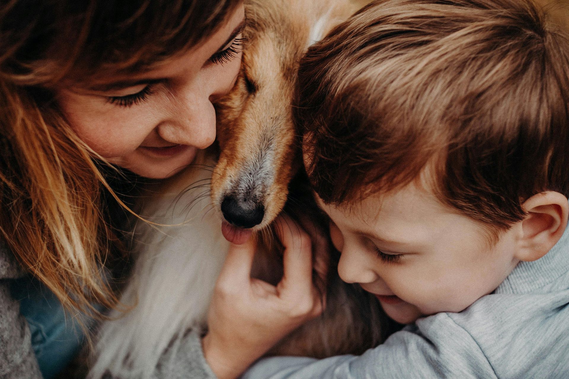 A woman and a child are hugging a dog.