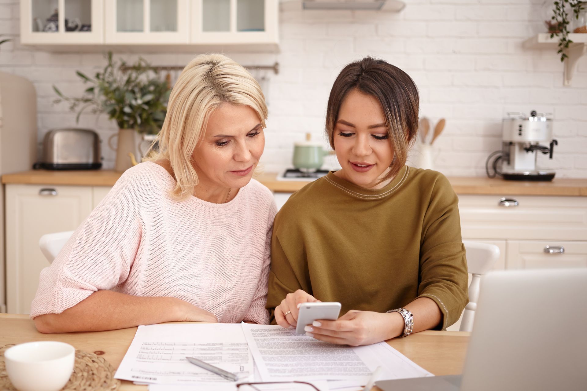 Two women are sitting at a table looking at a cell phone.