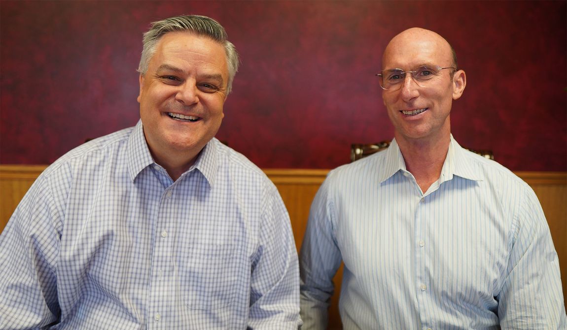 Two men are sitting next to each other and smiling for the camera.