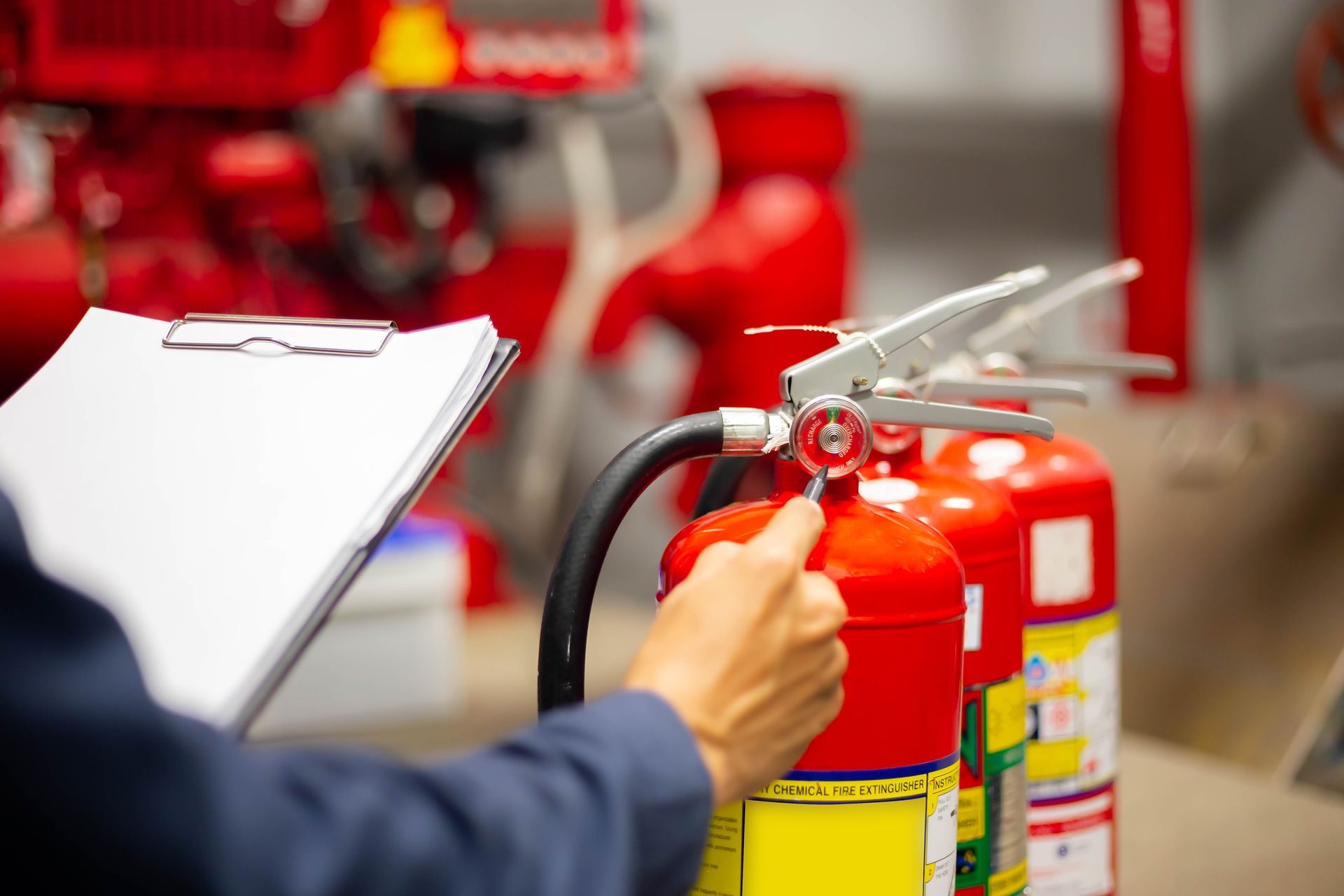 Person inspecting a red fire extinguisher in an industrial setting, holding a clipboard.