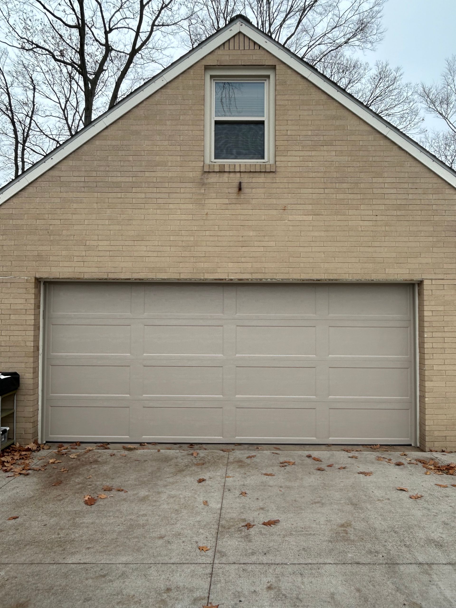 Tan brick garage with a closed, light-colored garage door and a small window above.