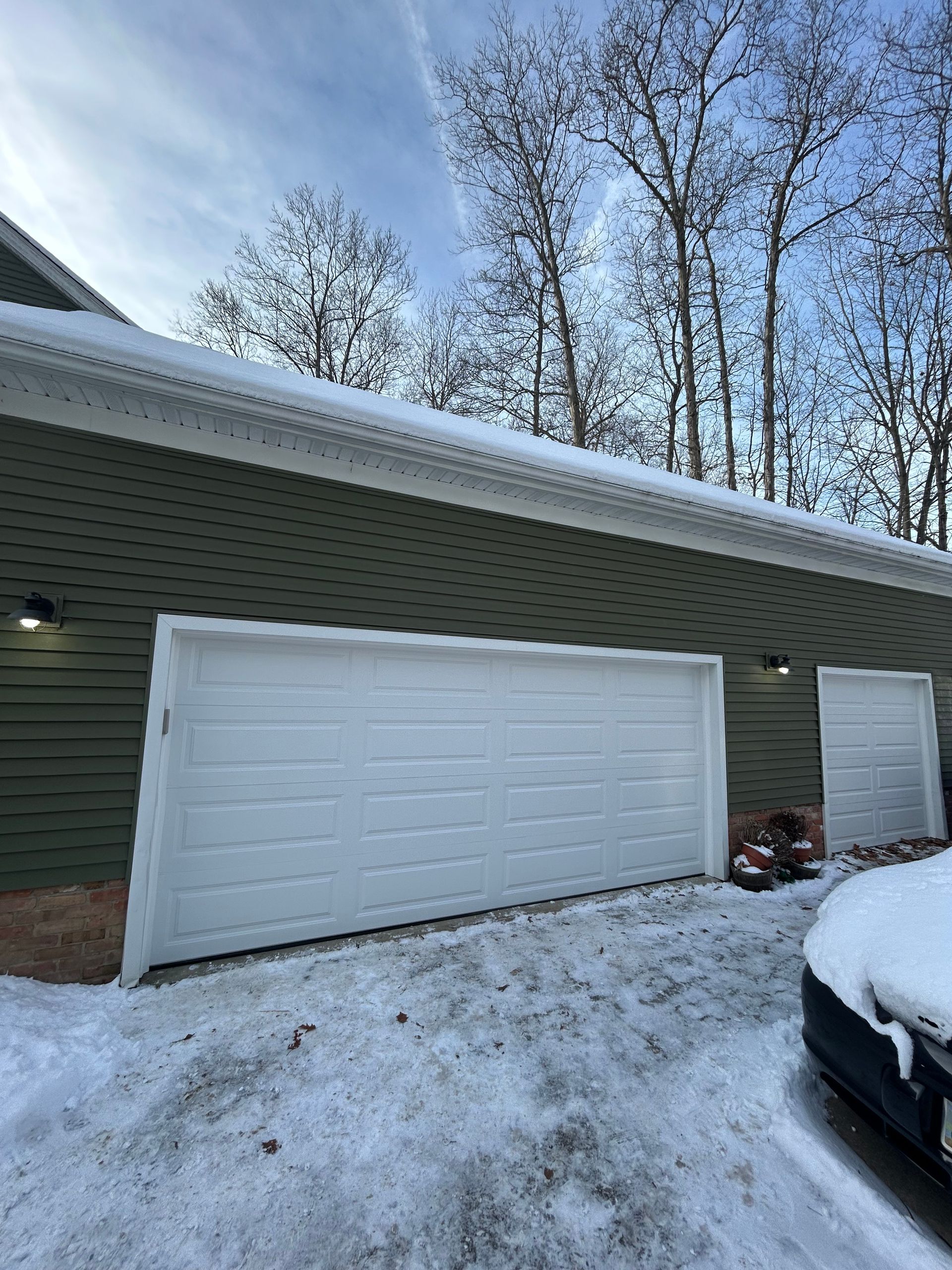 White garage door partially open on a green building with snow on the ground.