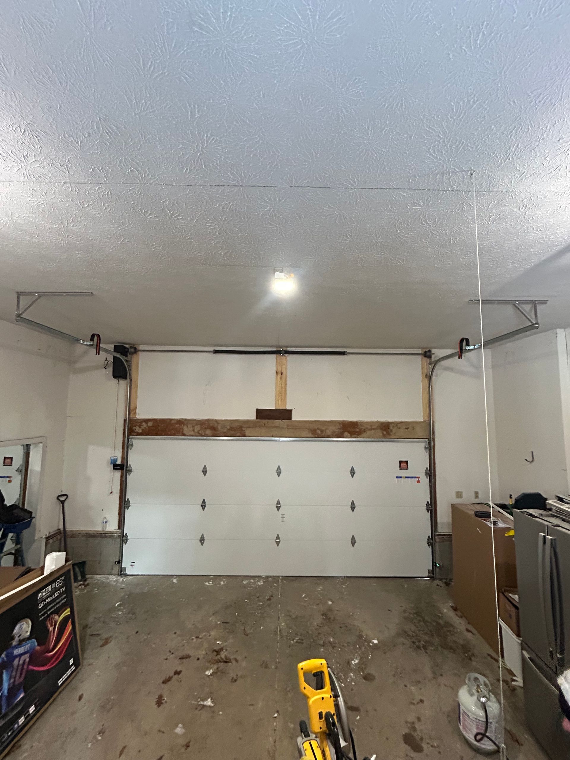 Garage interior, closed white garage door, concrete floor, overhead light, and construction tools.