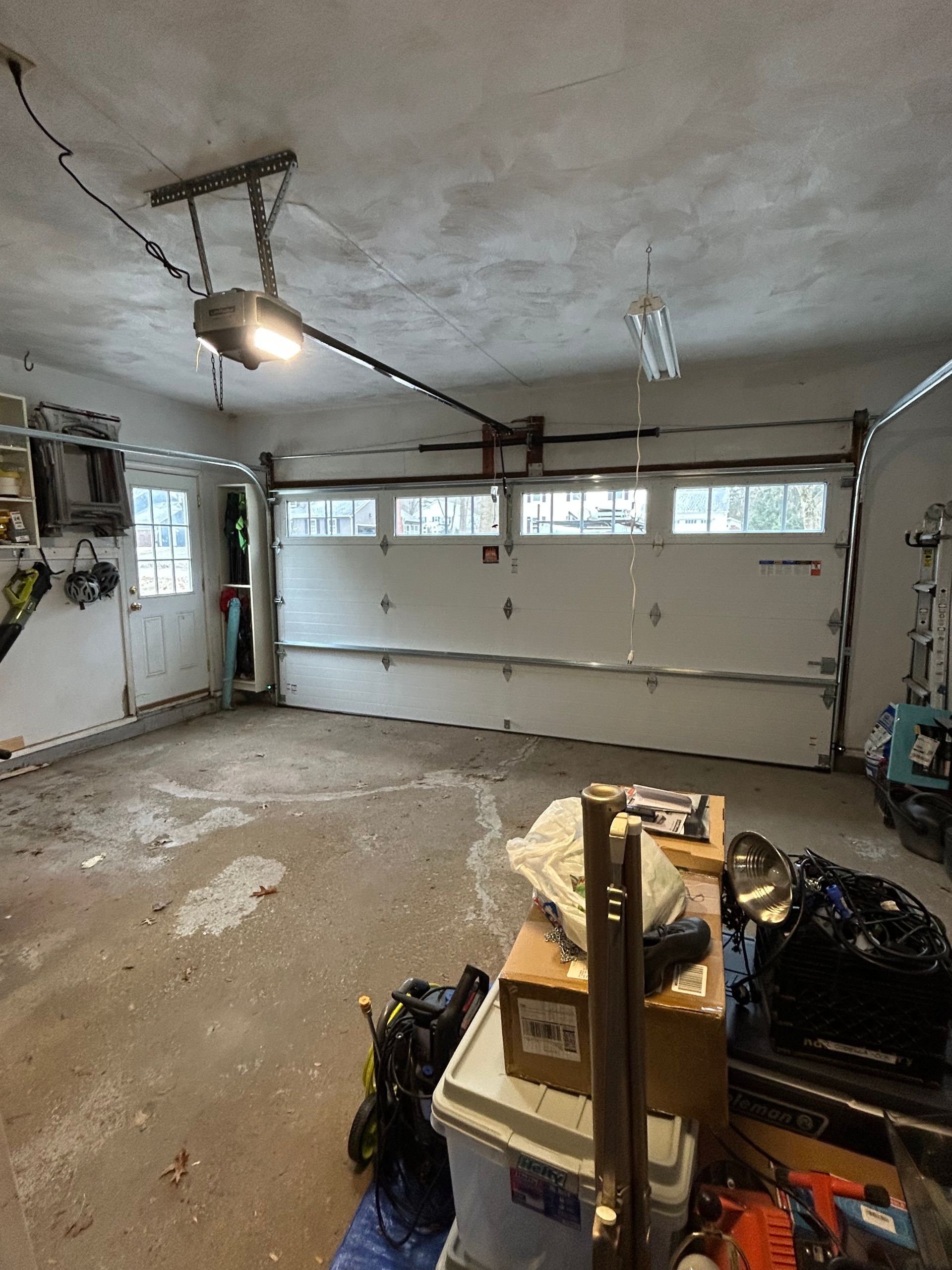 Garage interior with open garage door. Concrete floor and cluttered storage.