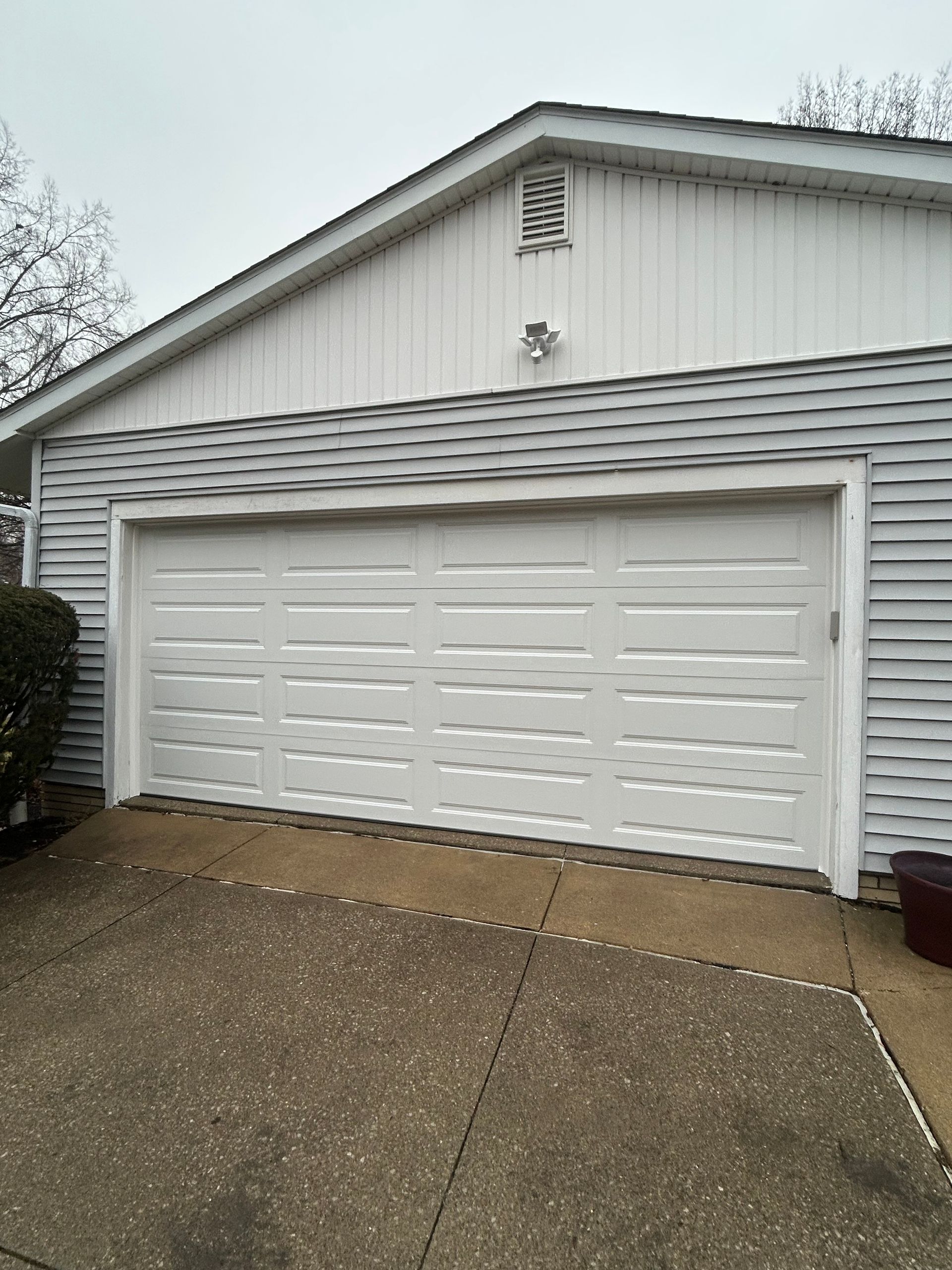 White garage with a closed, panelled door and gray siding.