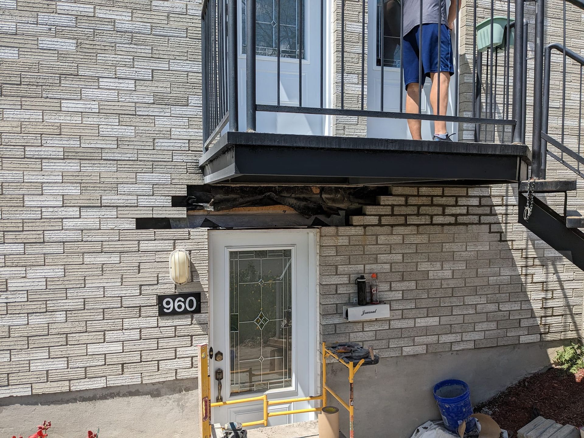 Un homme se tient sur le balcon d'un immeuble en briques.