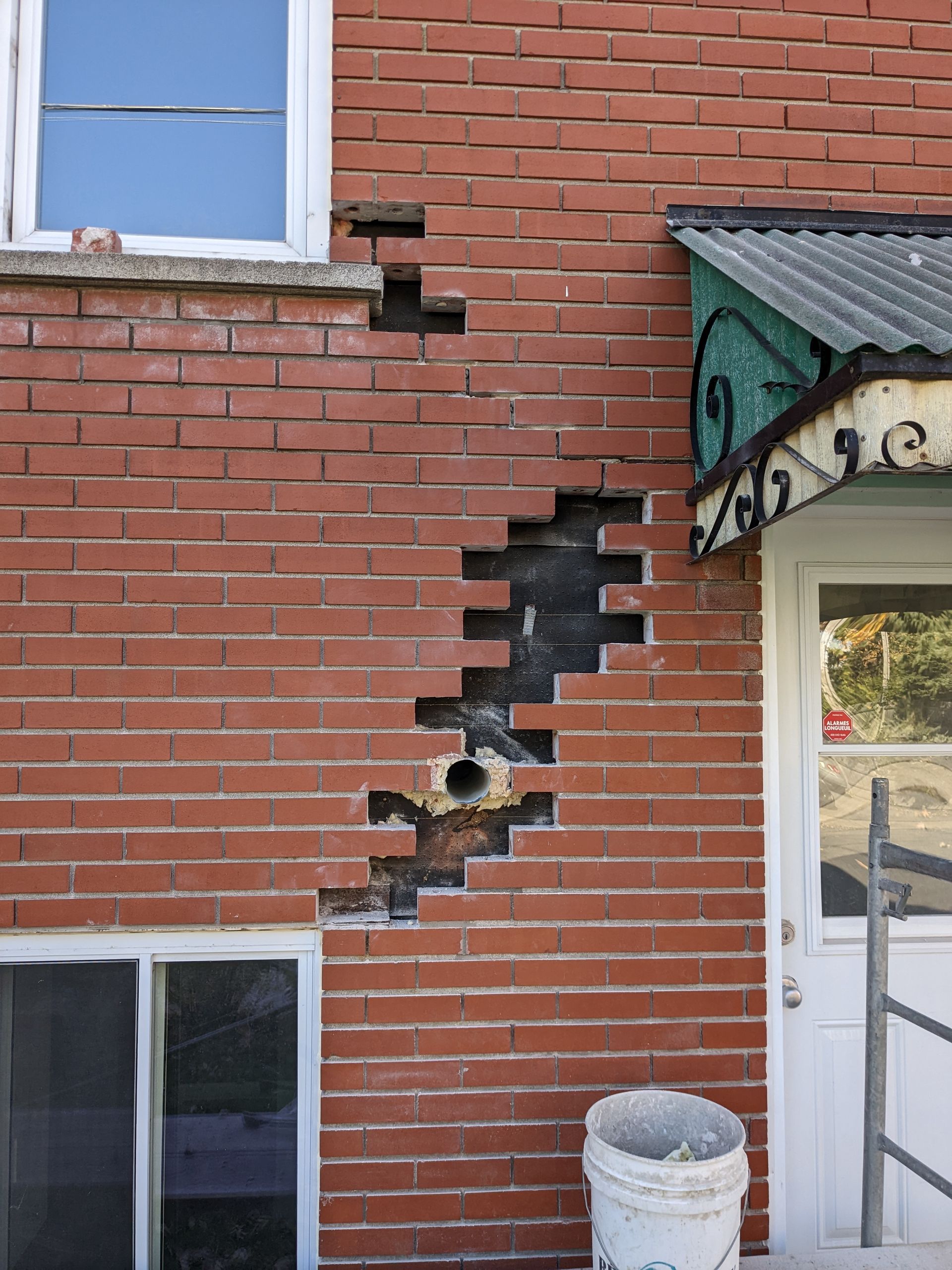 Un mur de briques avec un trou et un seau devant