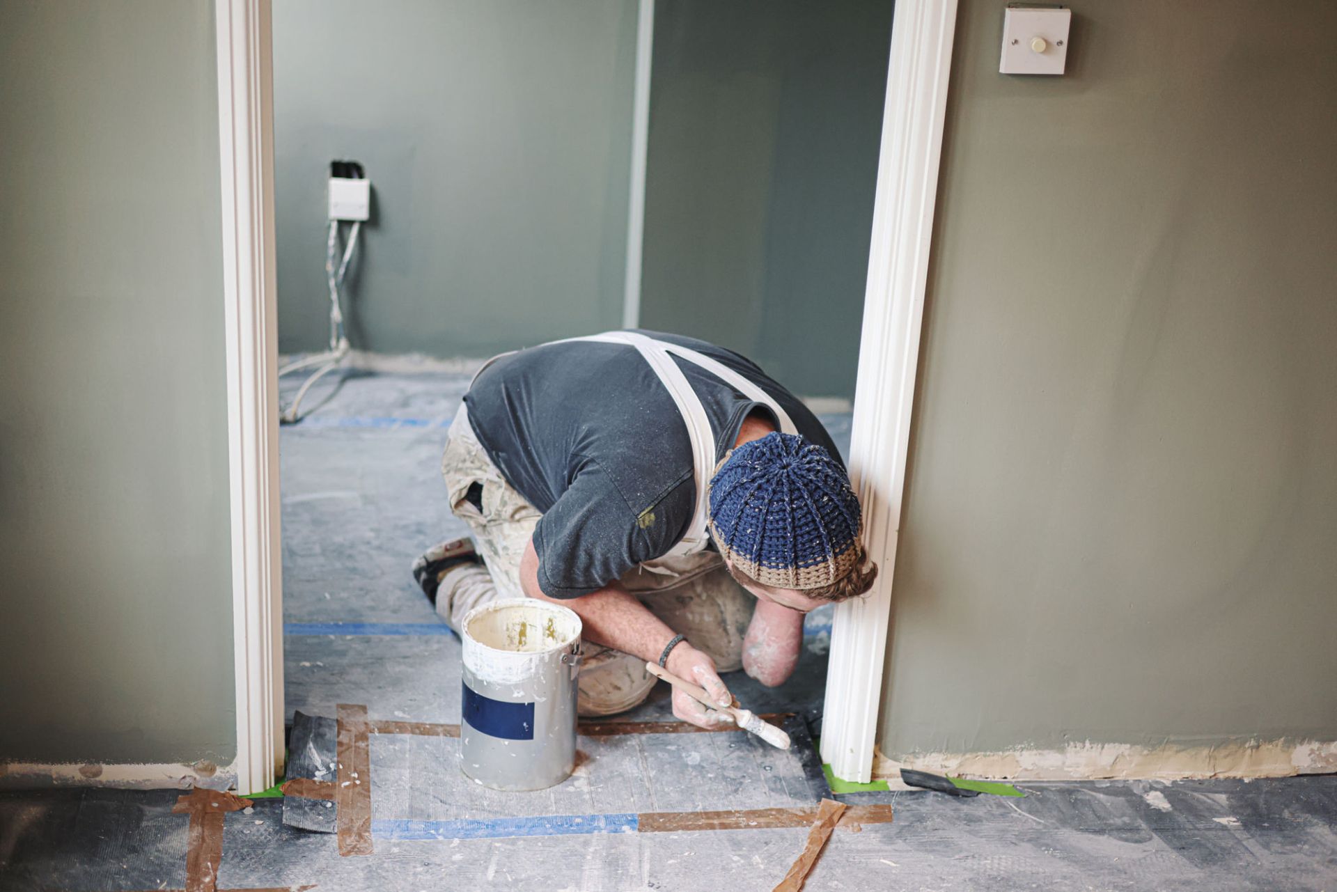 A man is kneeling down and painting a door in a room — Overland Park, KS — Johnson County Solutions