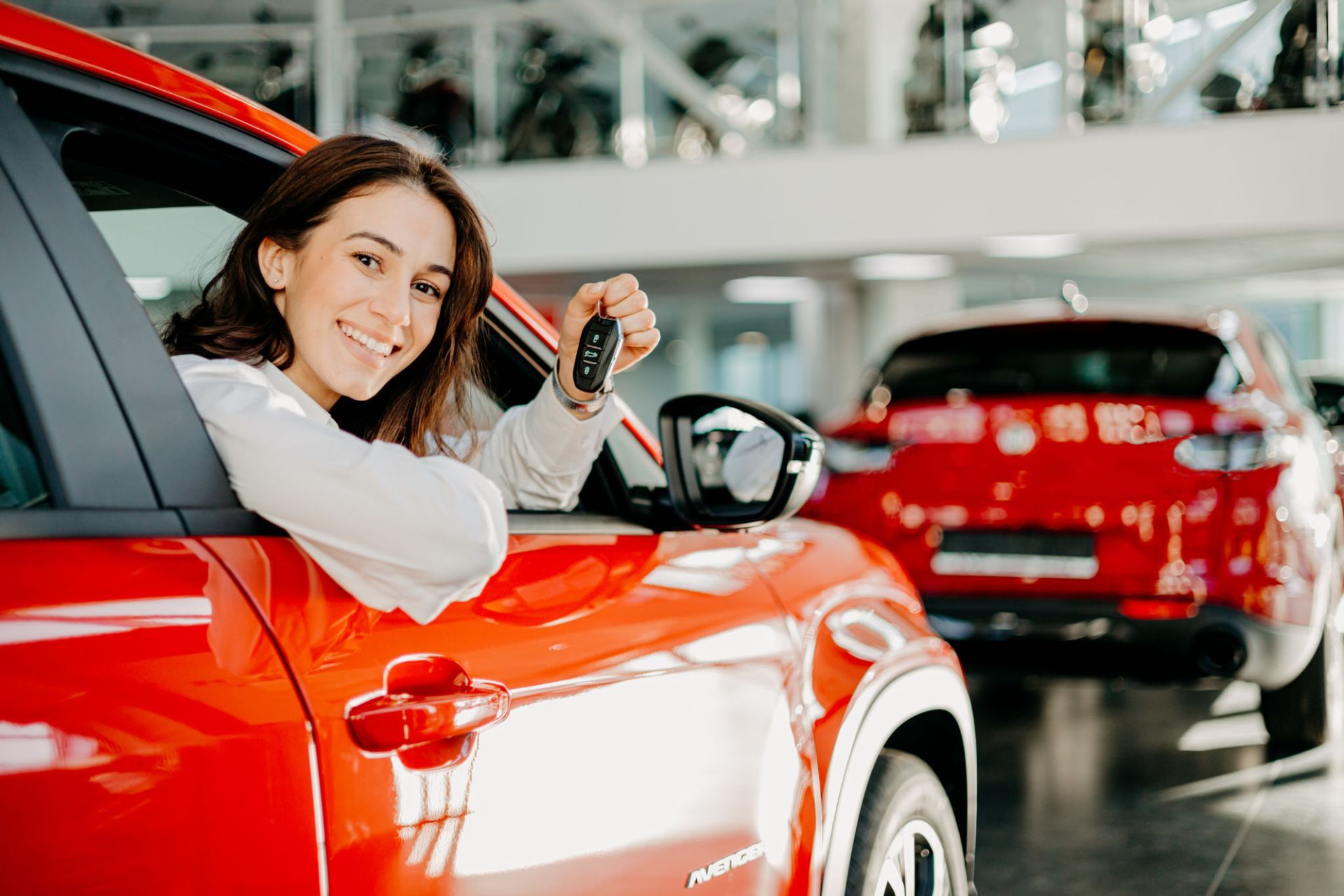 A woman is sitting in a red car holding a car key — Overland Park, KS — Johnson County Solutions