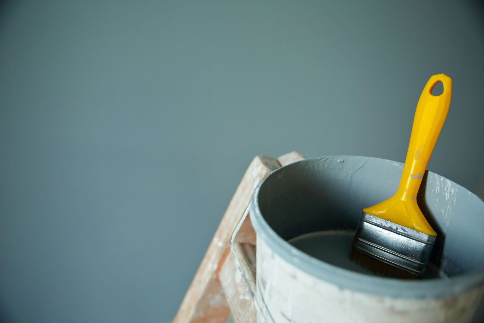 A yellow paint brush is sitting in a bucket of paint — Overland Park, KS — Johnson County Solutions