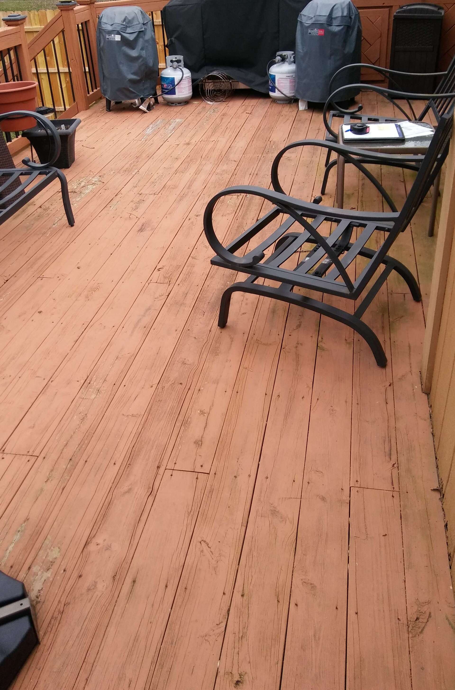 A wooden deck with chairs , a table and a grill.