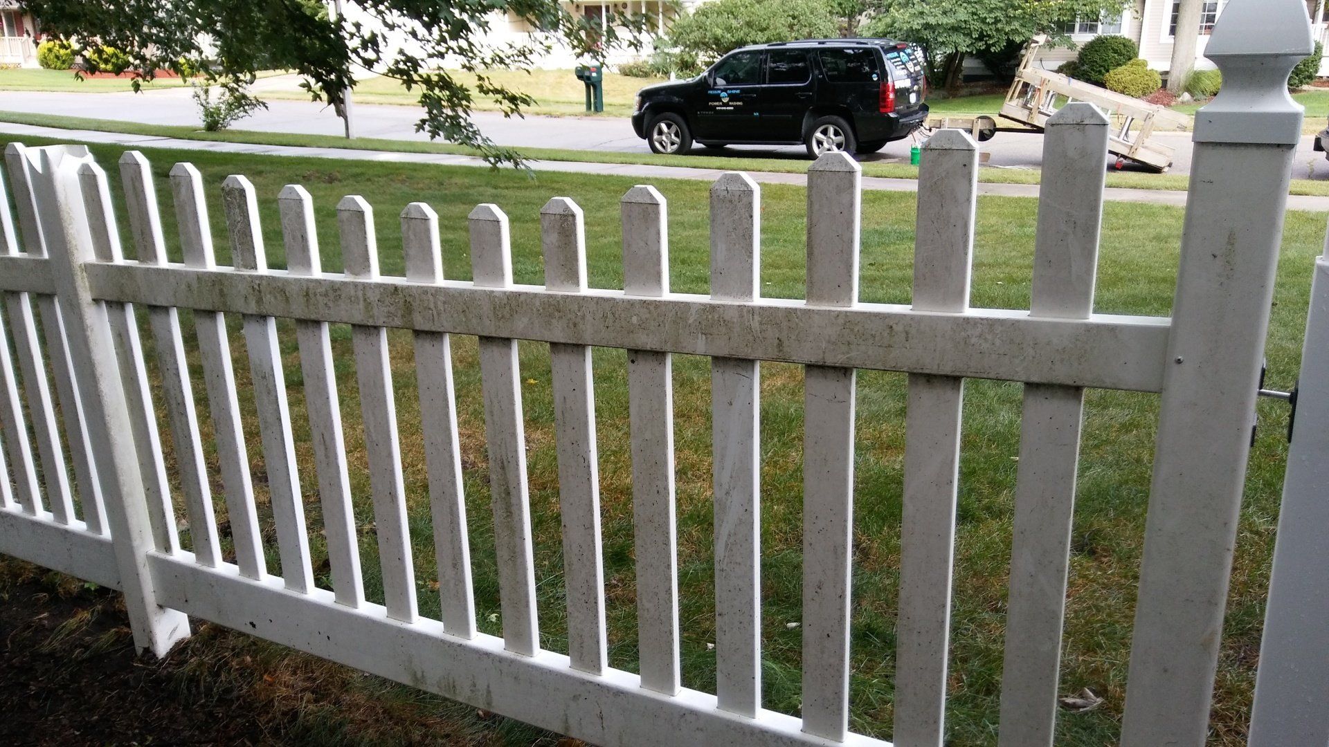 A white picket fence with a black suv parked behind it