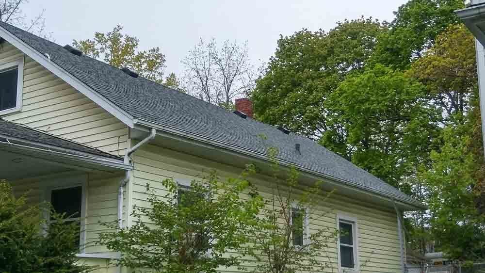 A white house with a gray roof is surrounded by trees.