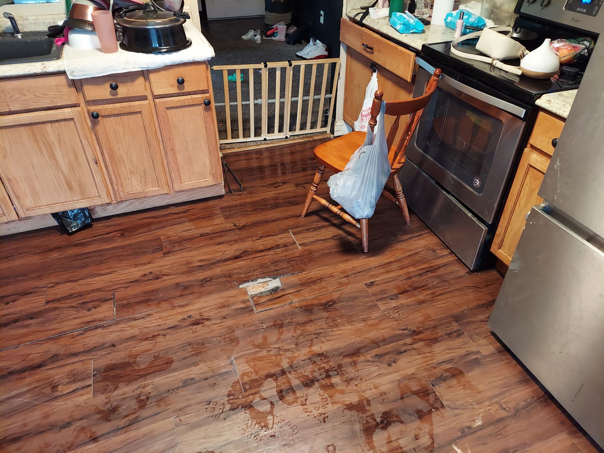 A kitchen with wooden floors , a stove , a refrigerator , and a chair.