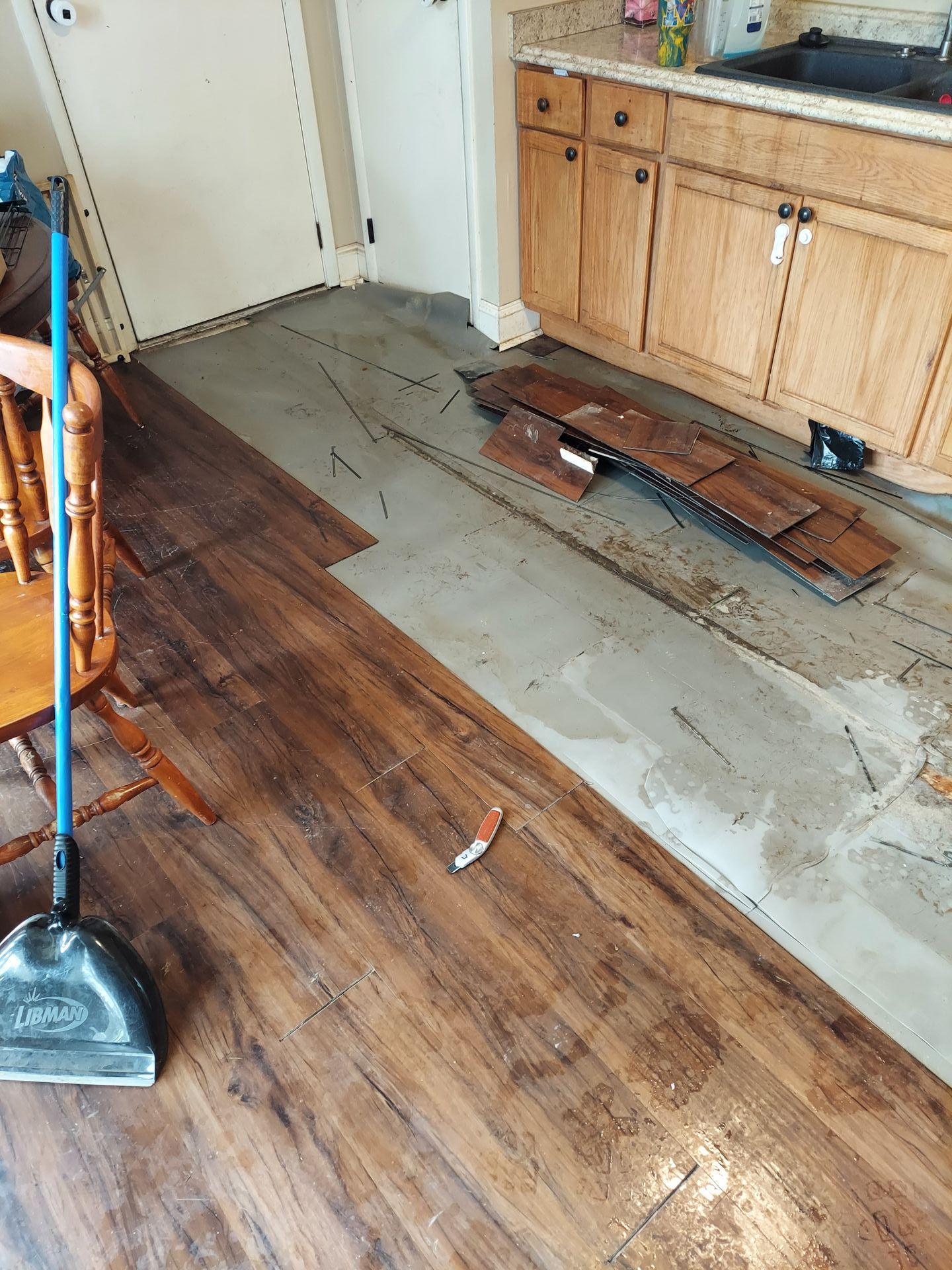 A broom is sitting on a wooden floor in a kitchen.