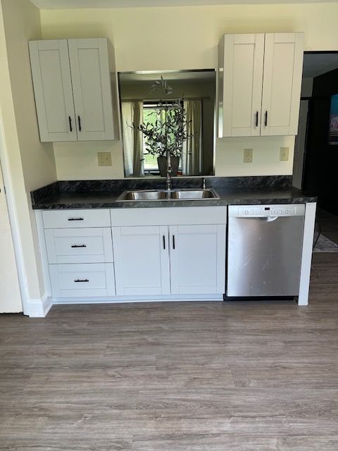 A kitchen with white cabinets , a sink , and a stainless steel dishwasher.