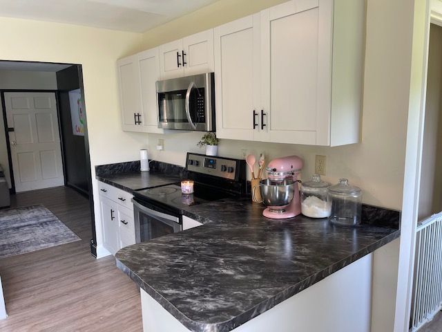 A kitchen with white cabinets , black counter tops , a stove , microwave , and a pink mixer.