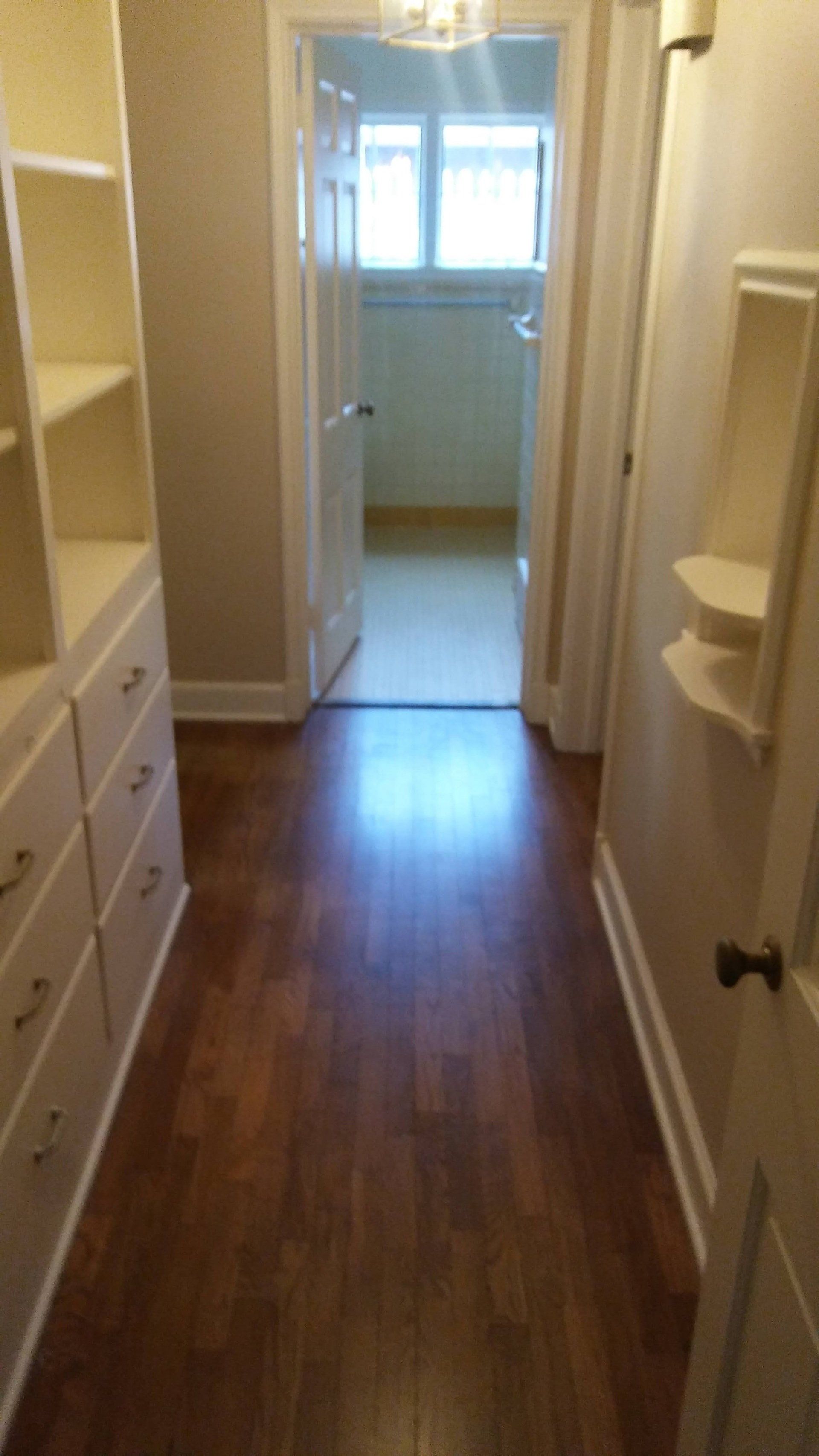 A hallway with hardwood floors and shelves leading to a bathroom.