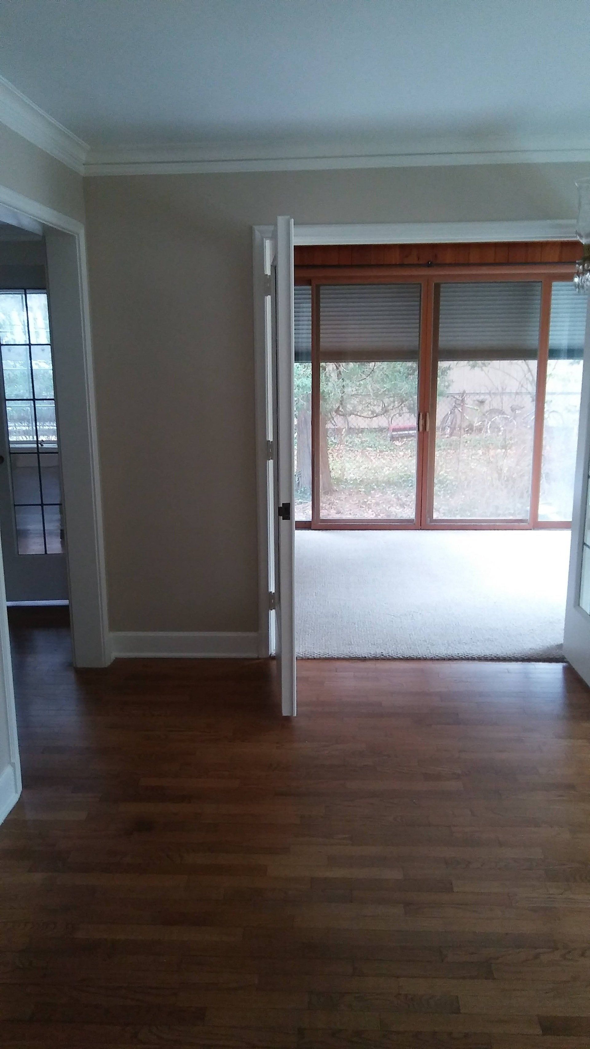 An empty living room with hardwood floors and sliding glass doors leading to a screened in porch.
