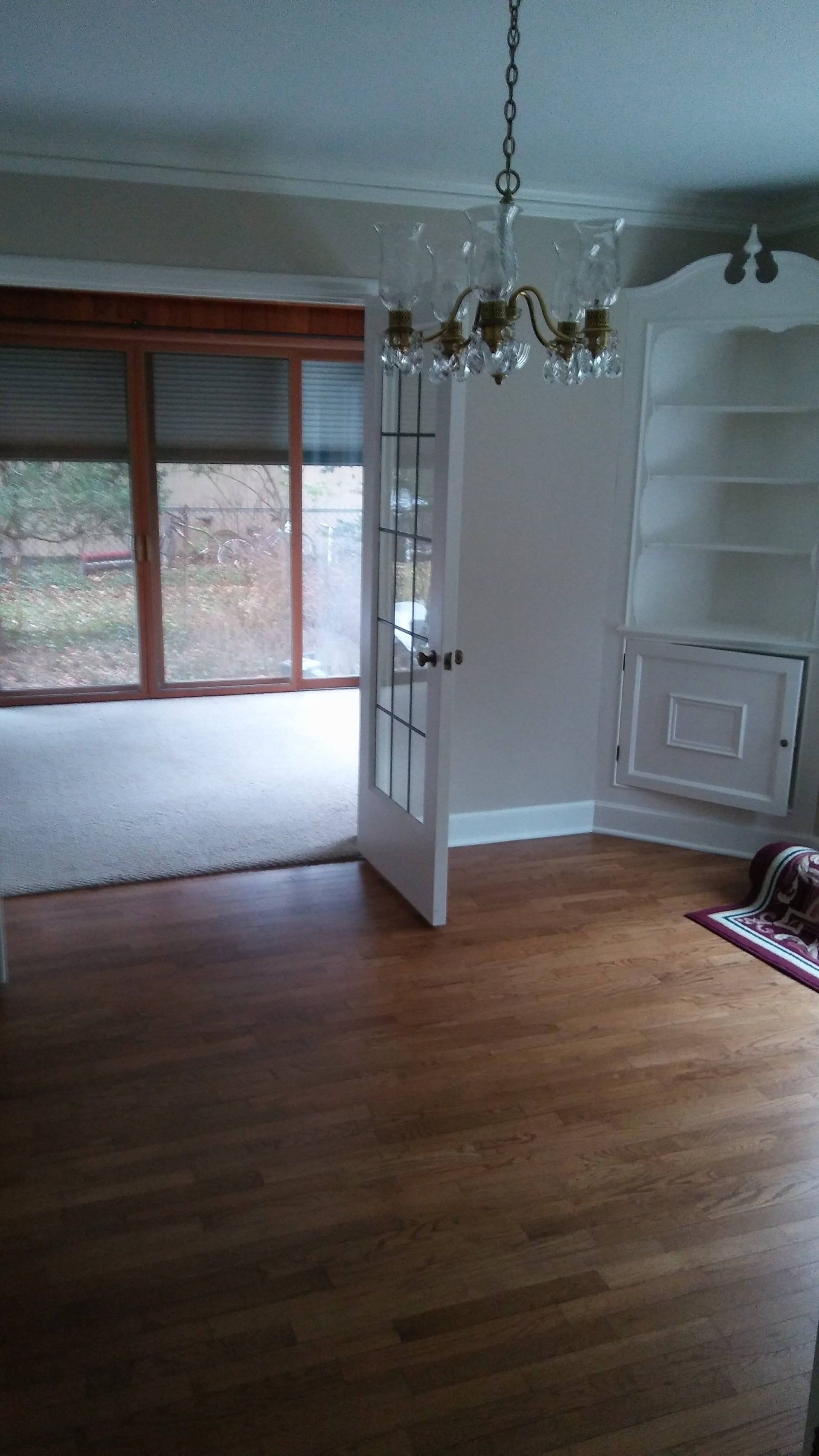An empty living room with hardwood floors and a chandelier.