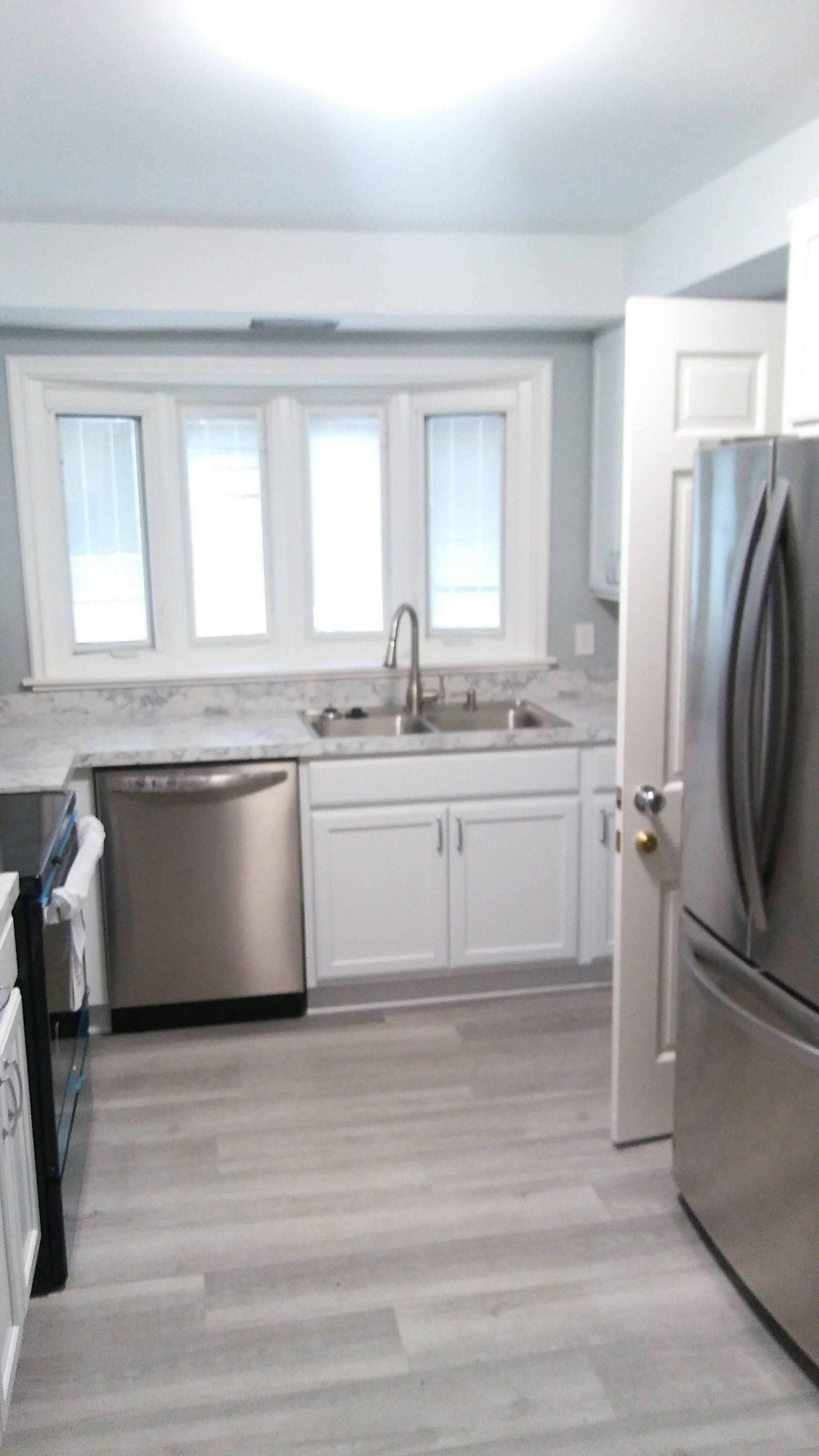 A kitchen with stainless steel appliances , white cabinets , a sink , and a refrigerator.