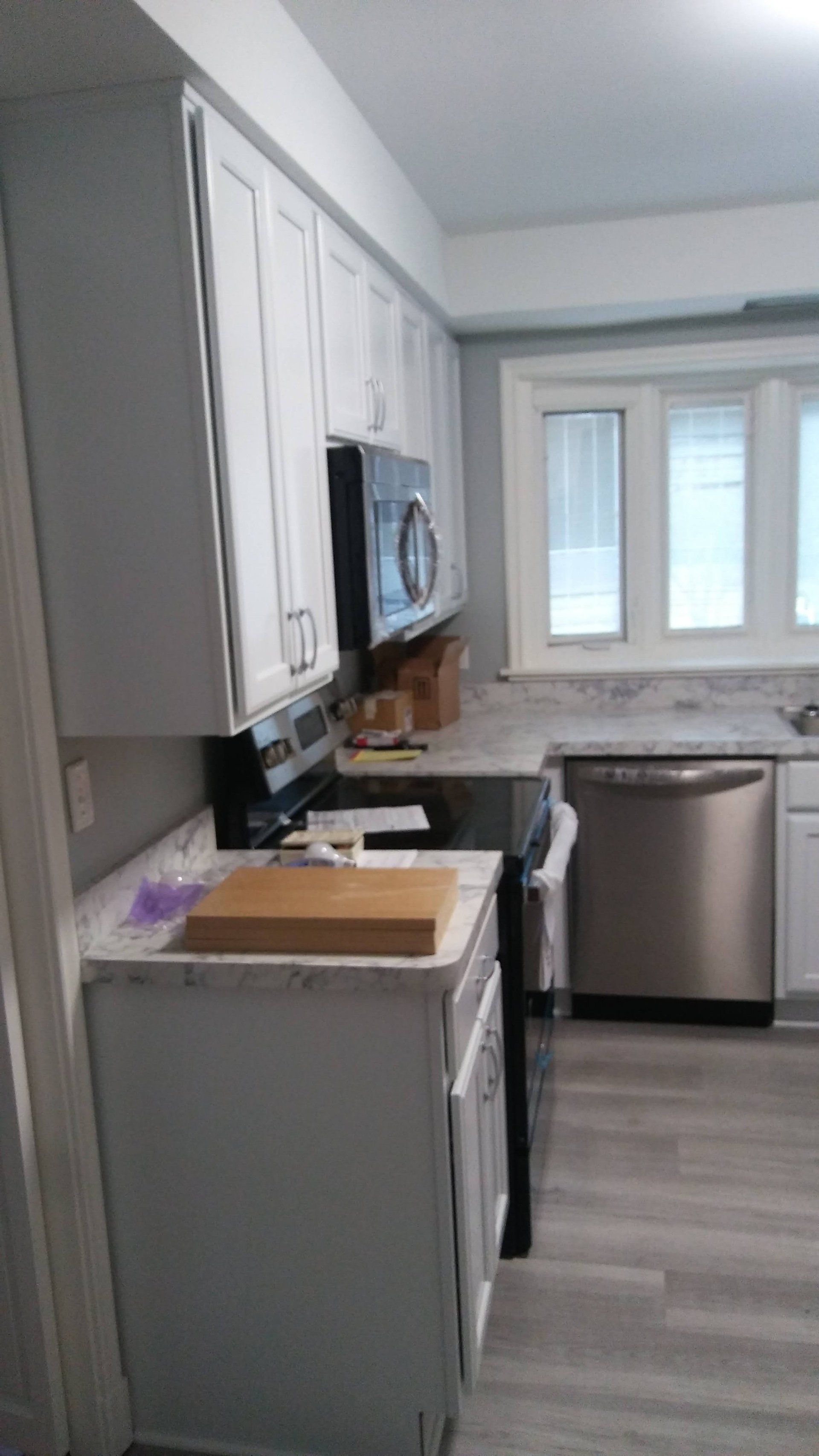 A kitchen with white cabinets , a stove , a microwave , and a dishwasher.