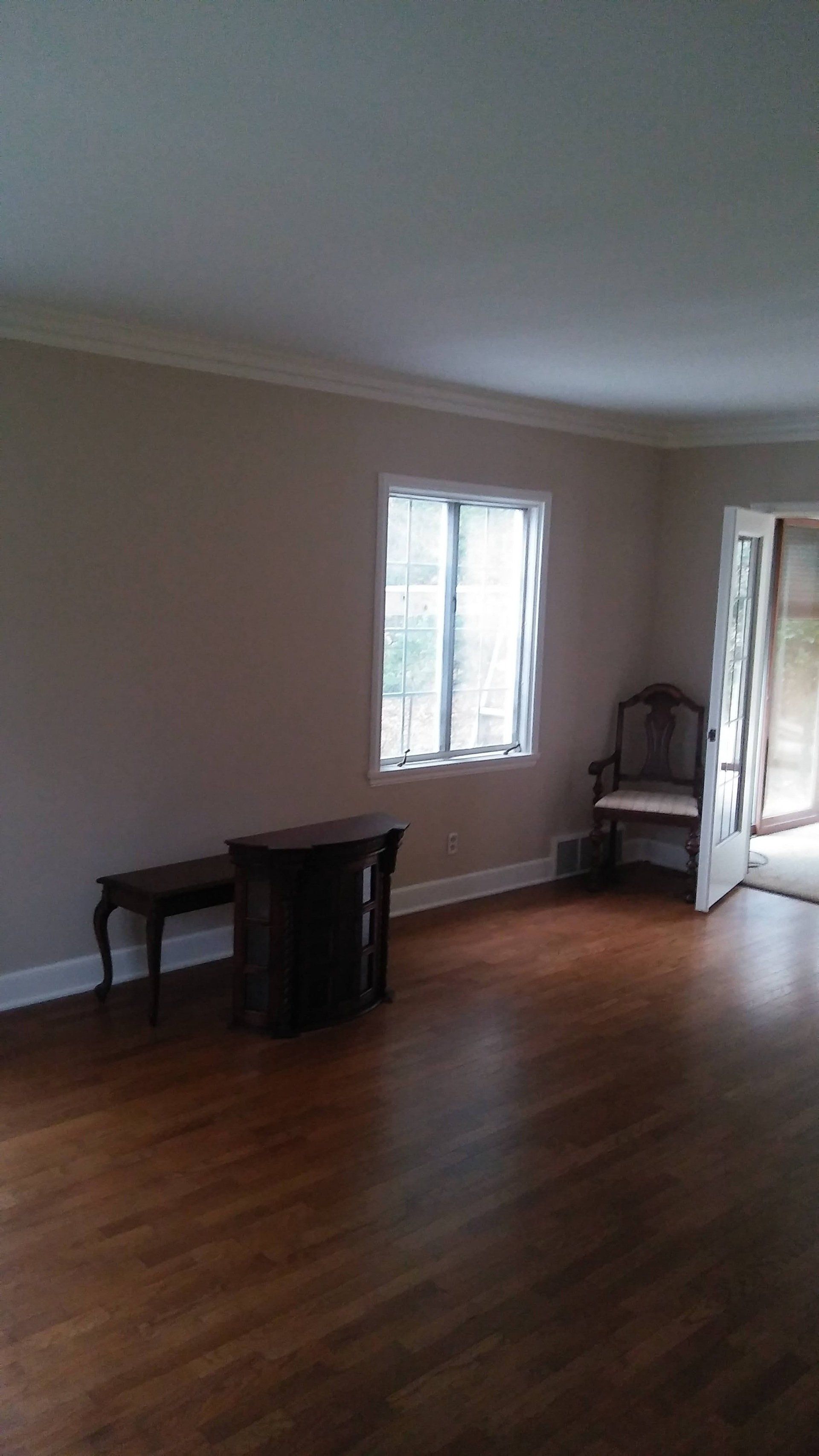 An empty living room with hardwood floors , a chair , a table and a window.