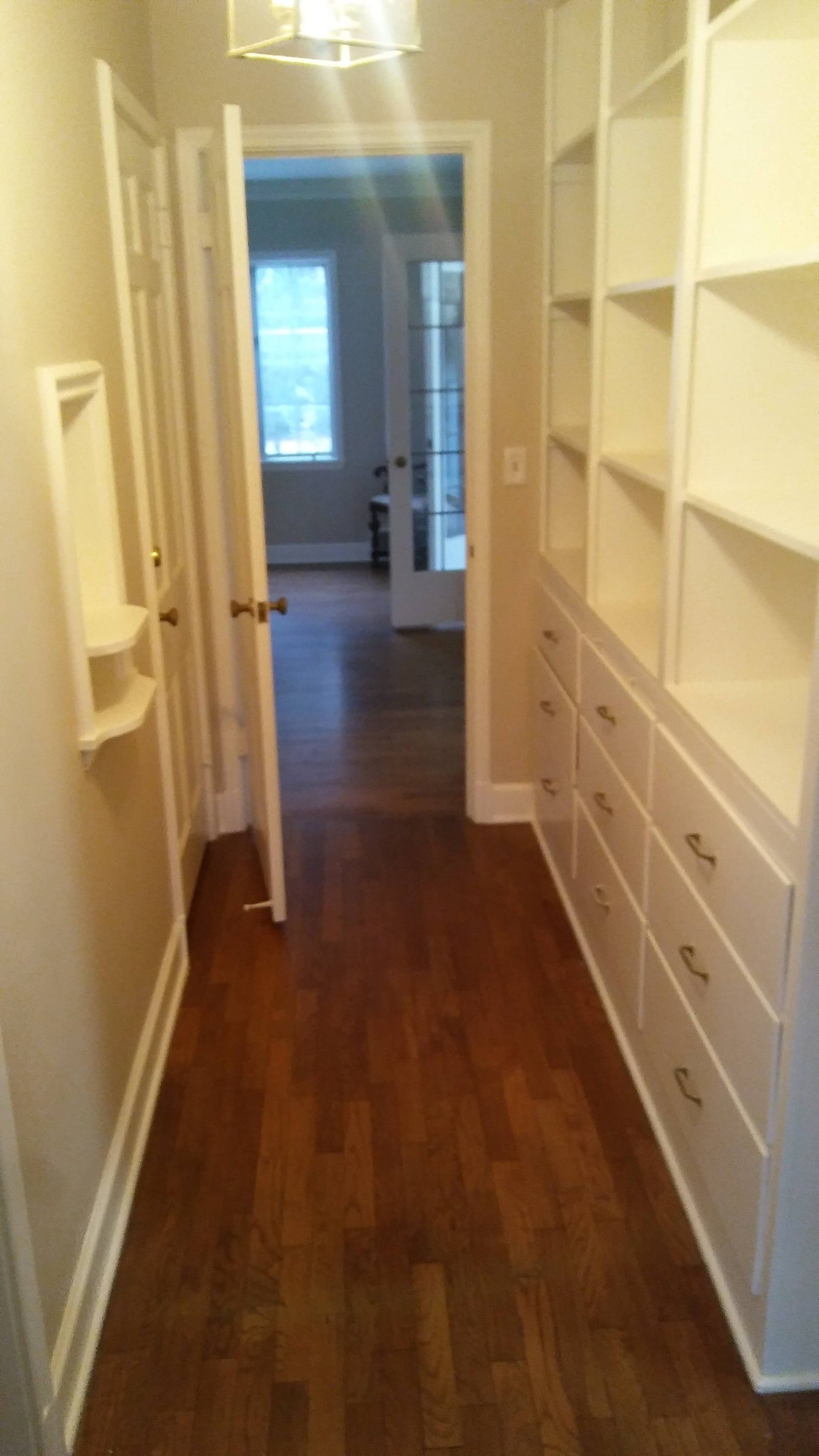 A hallway with lots of shelves and drawers in a house.