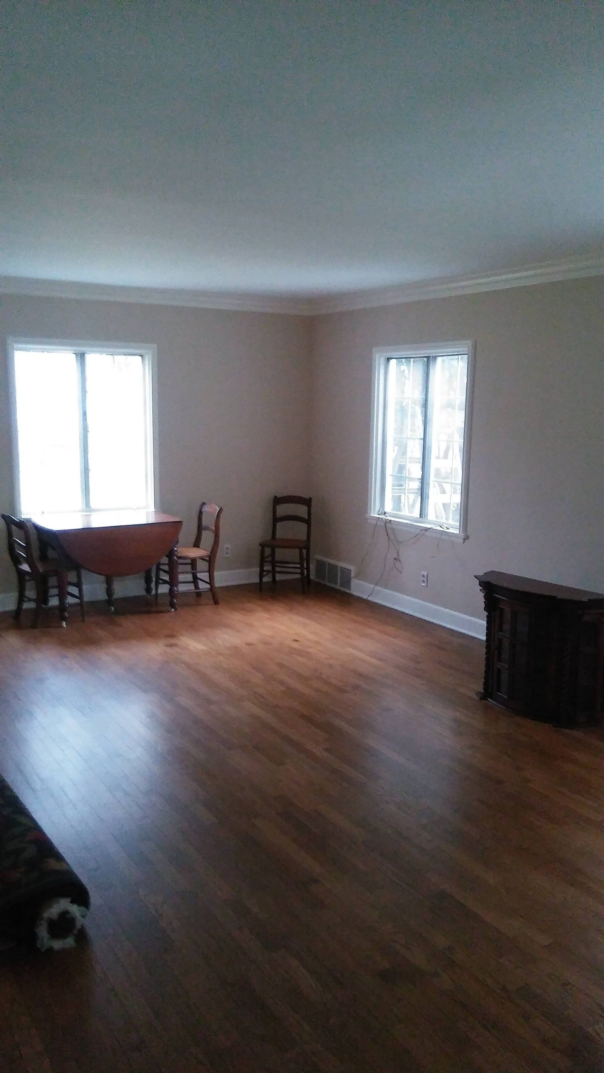 An empty living room with hardwood floors and a table and chairs.