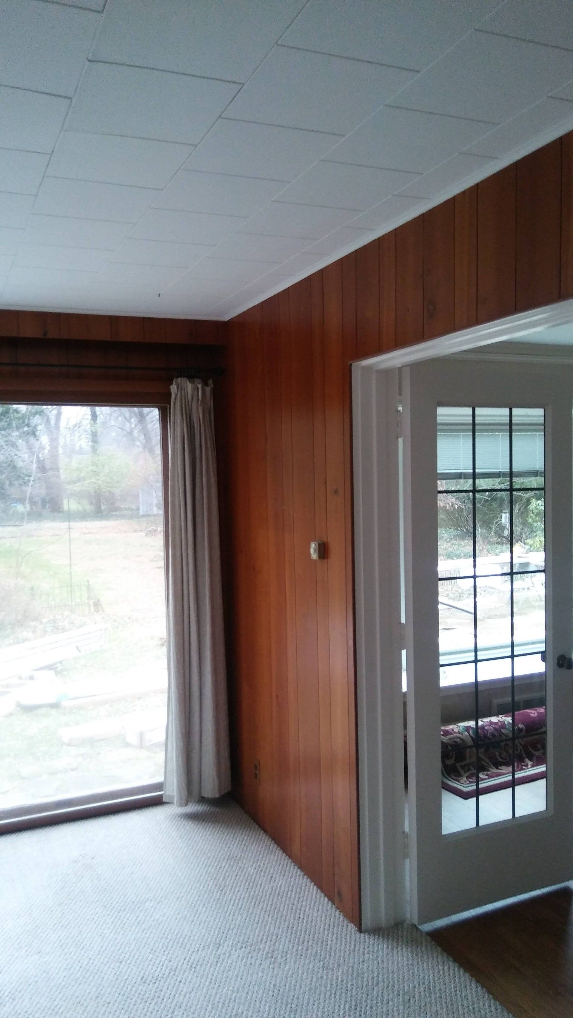 A living room with wood paneling and a large window.