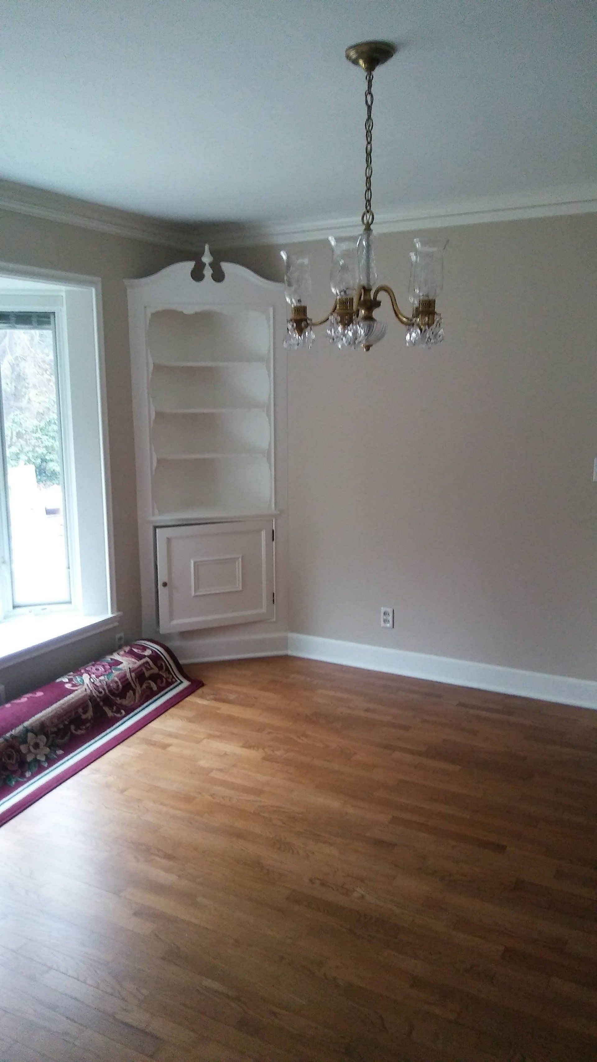 An empty living room with hardwood floors and a chandelier hanging from the ceiling.
