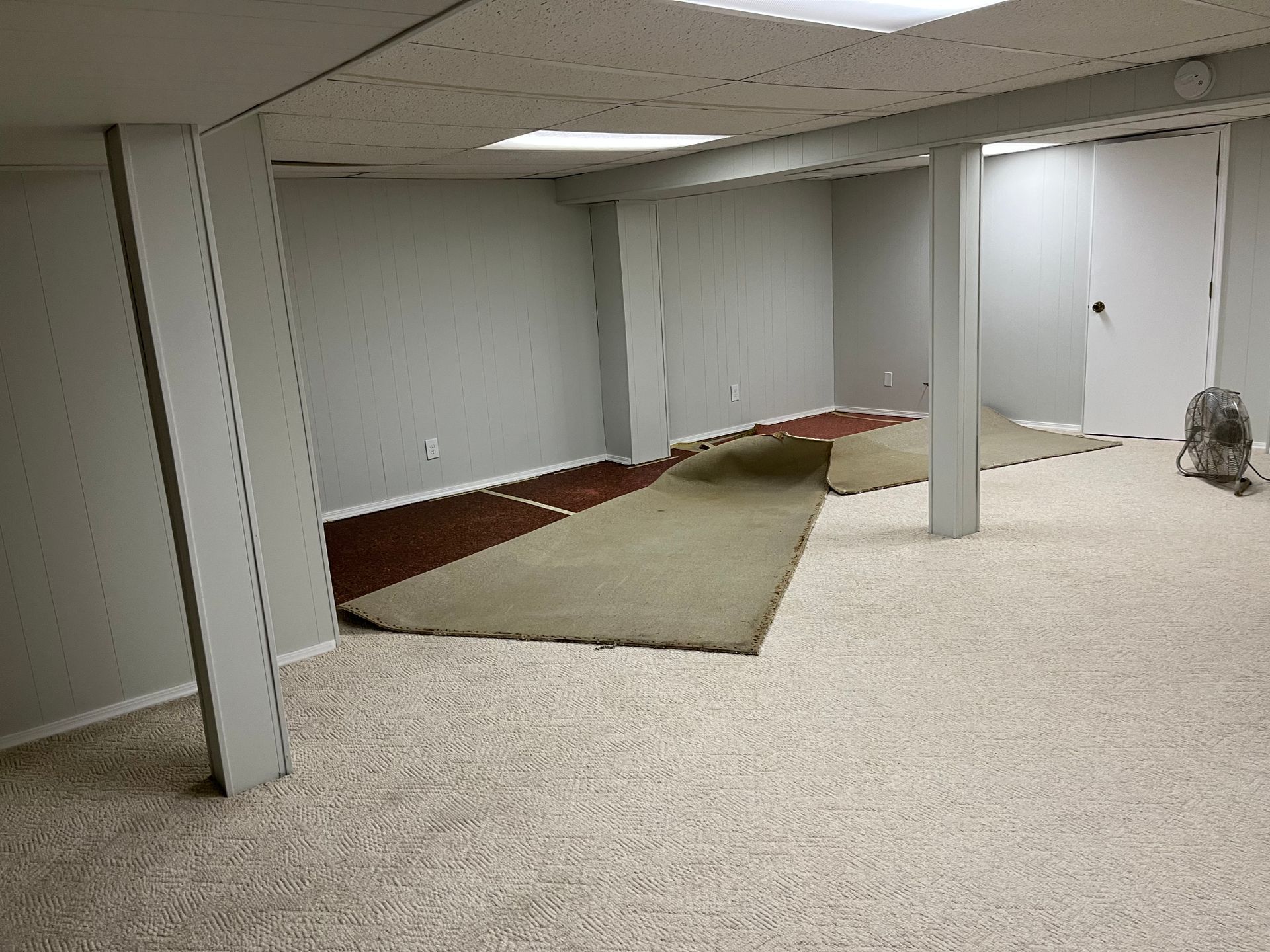 An empty basement with a fan and a rug on the floor.