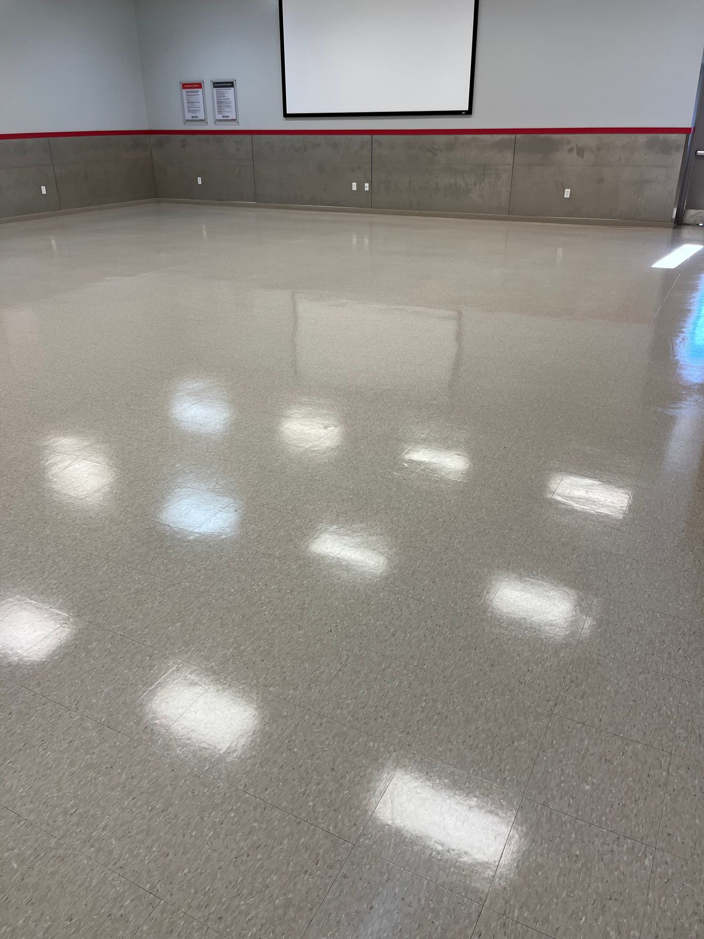 A large room with a projector screen on the wall and a shiny floor.
