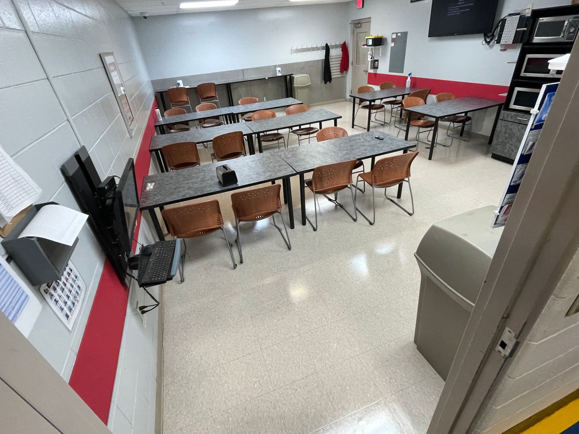 A classroom with tables and chairs and a trash can