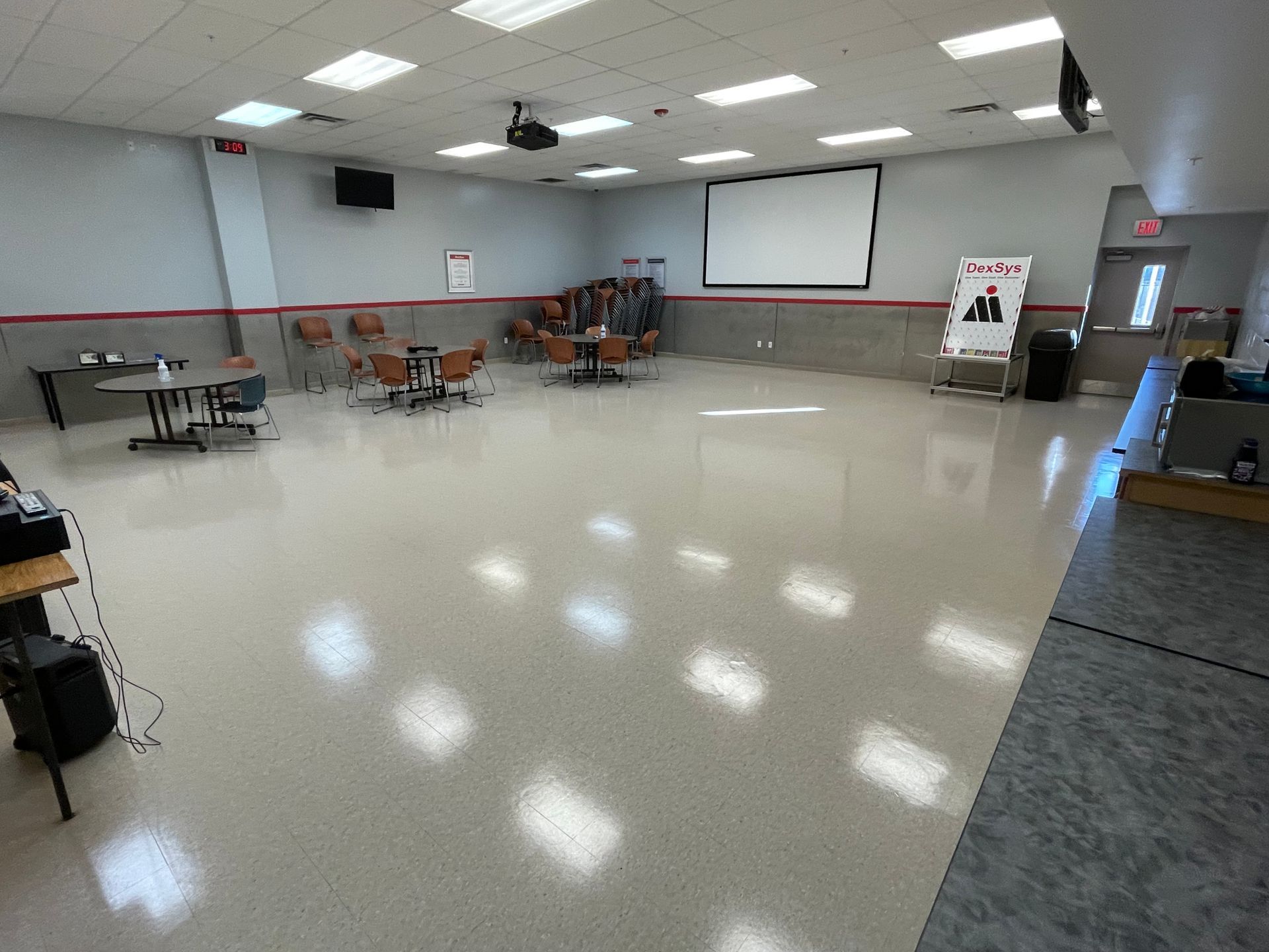 A large room with tables and chairs and a projector screen.